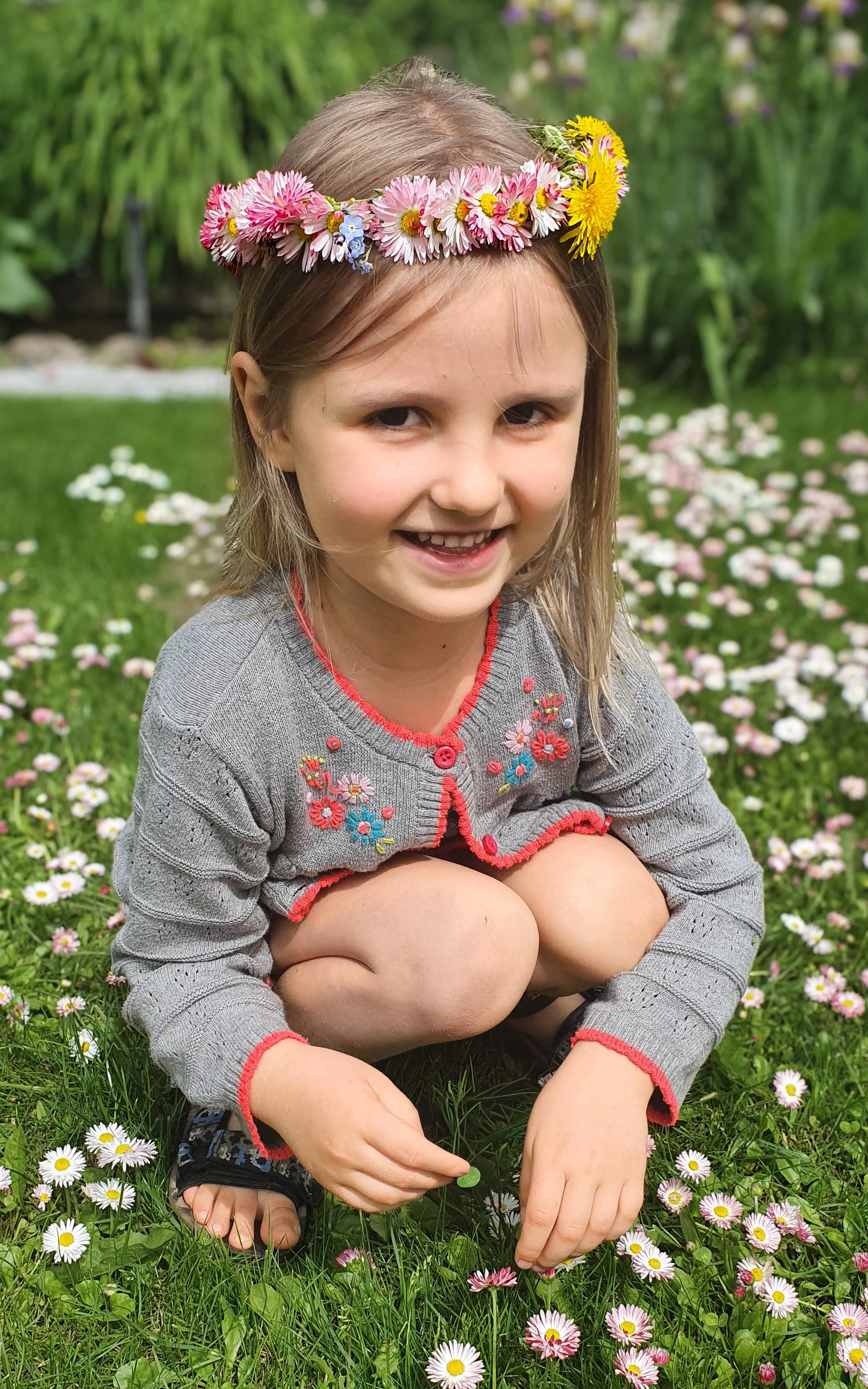 A beautiful, natural light portrait of a young girl wearing a delicate flower crown while sitting in a field of blooming daisies.
