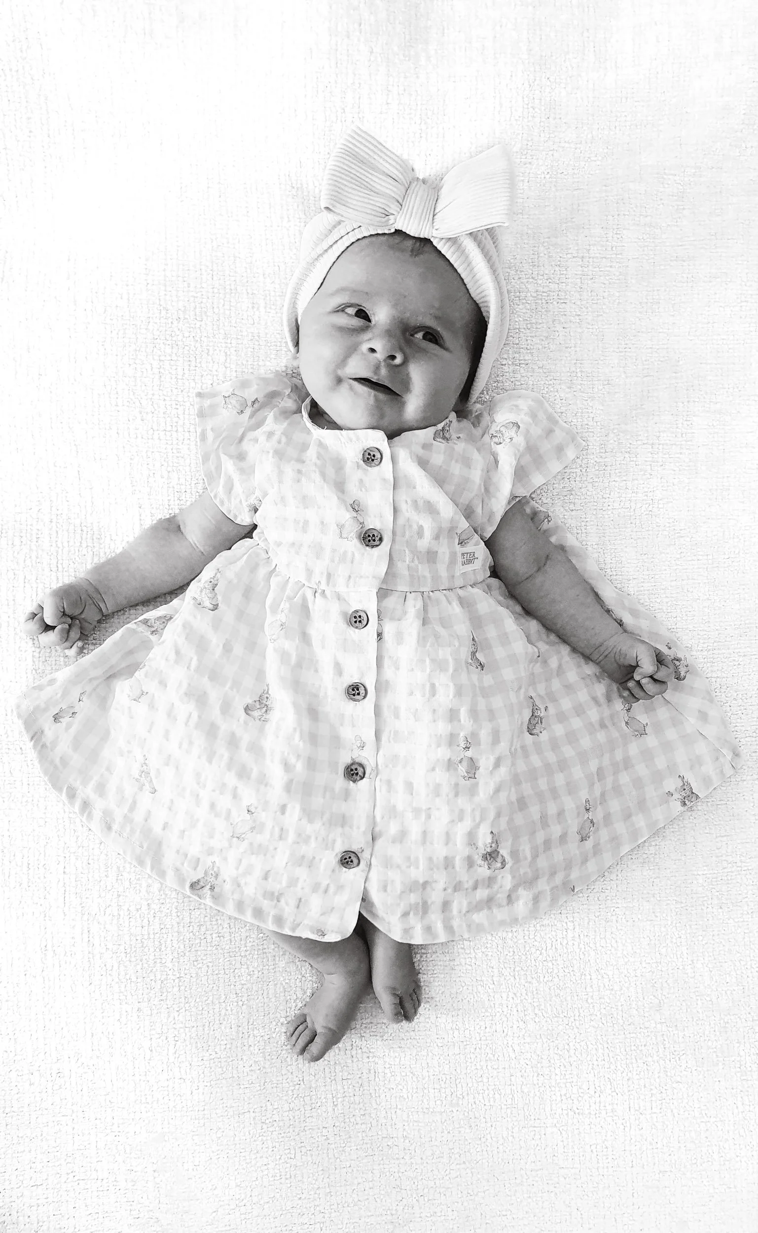 Newborn smiling in her little dress and big bow during in-home newborn photoshoot in Camberley.