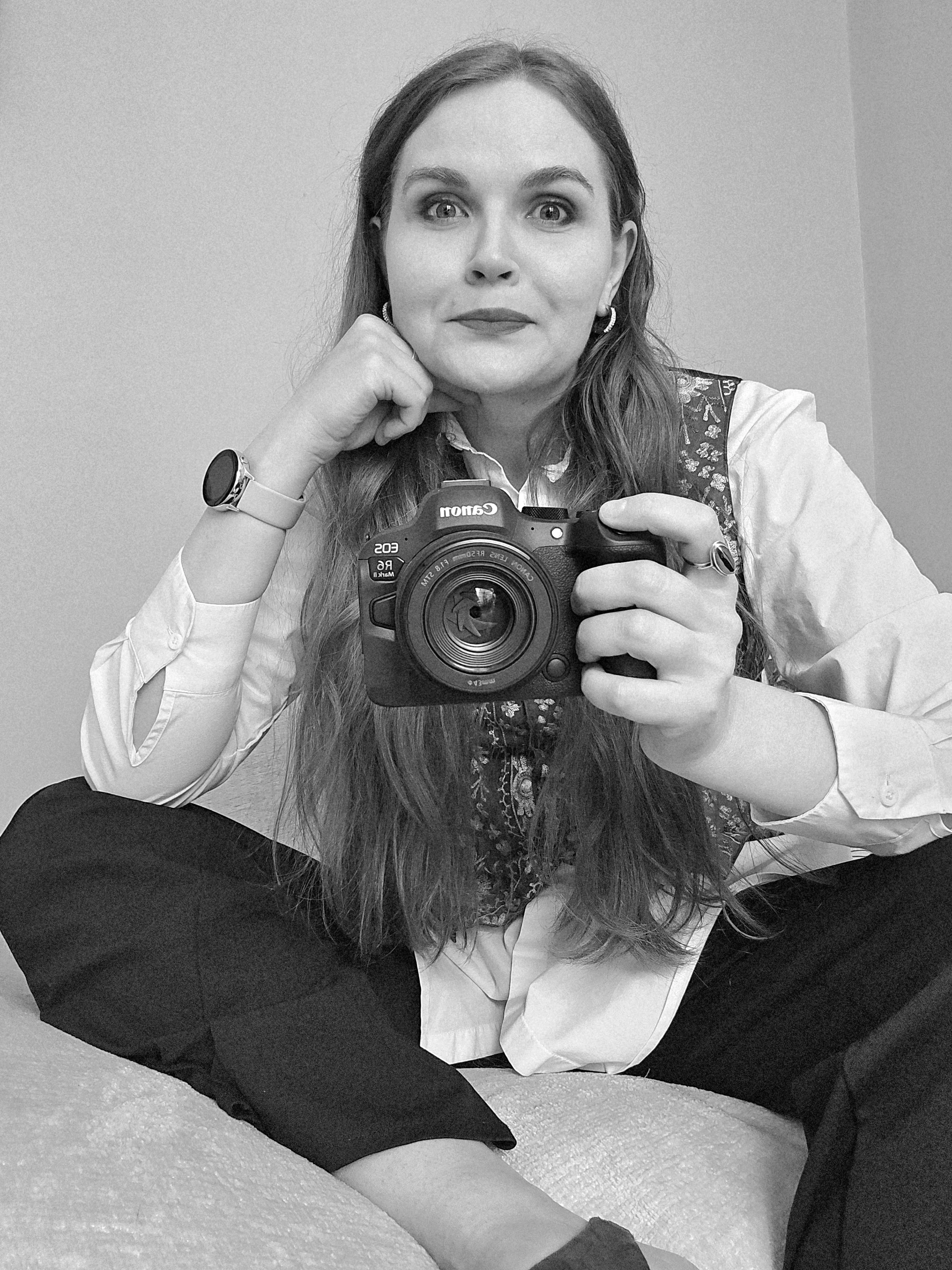 A casual, friendly selfie of a professional female photographer sitting comfortably on a sofa while holding her camera.