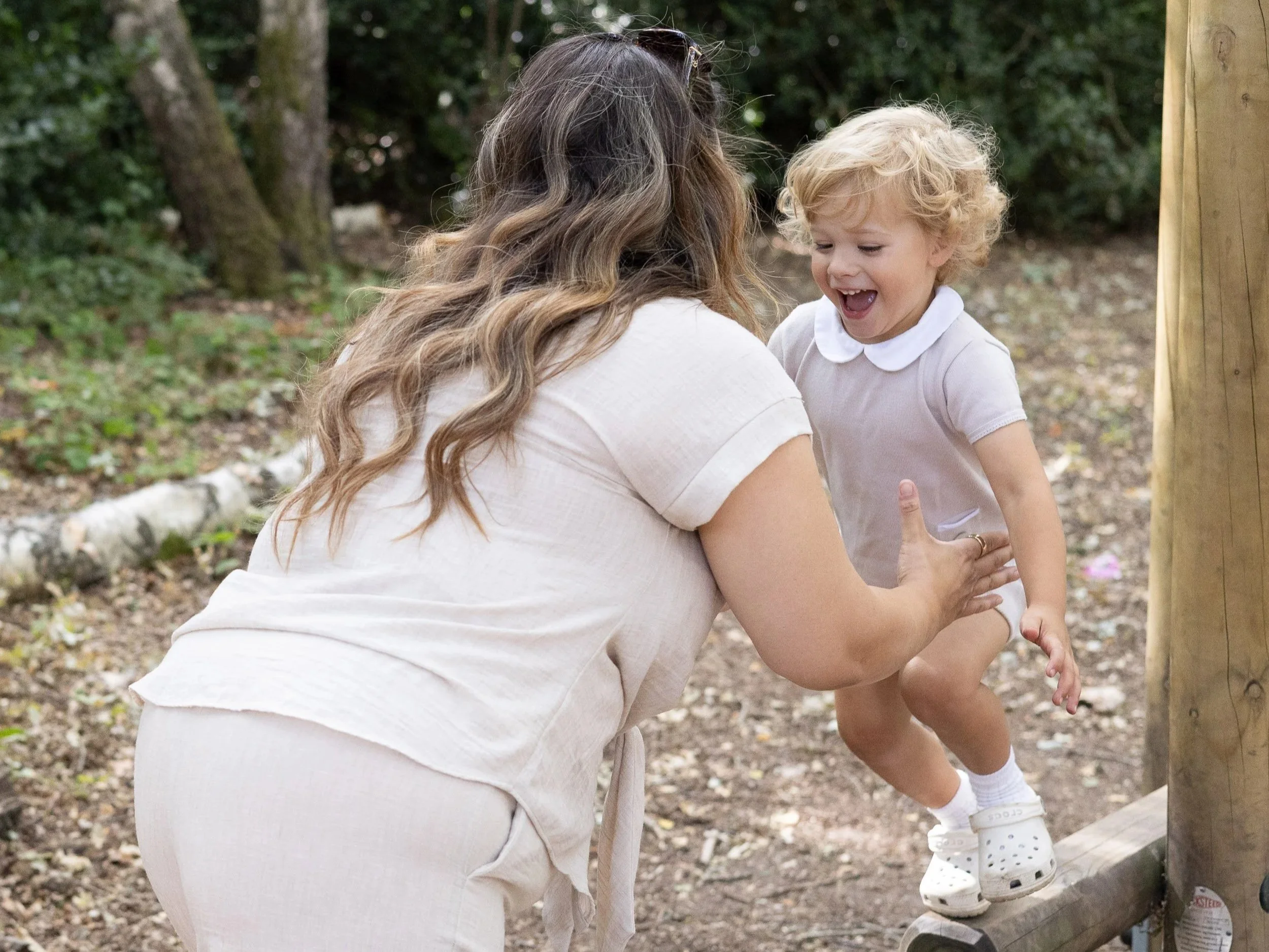 Mother playing and kneeling down with her toddler outdoors in a natural park setting in Surrey