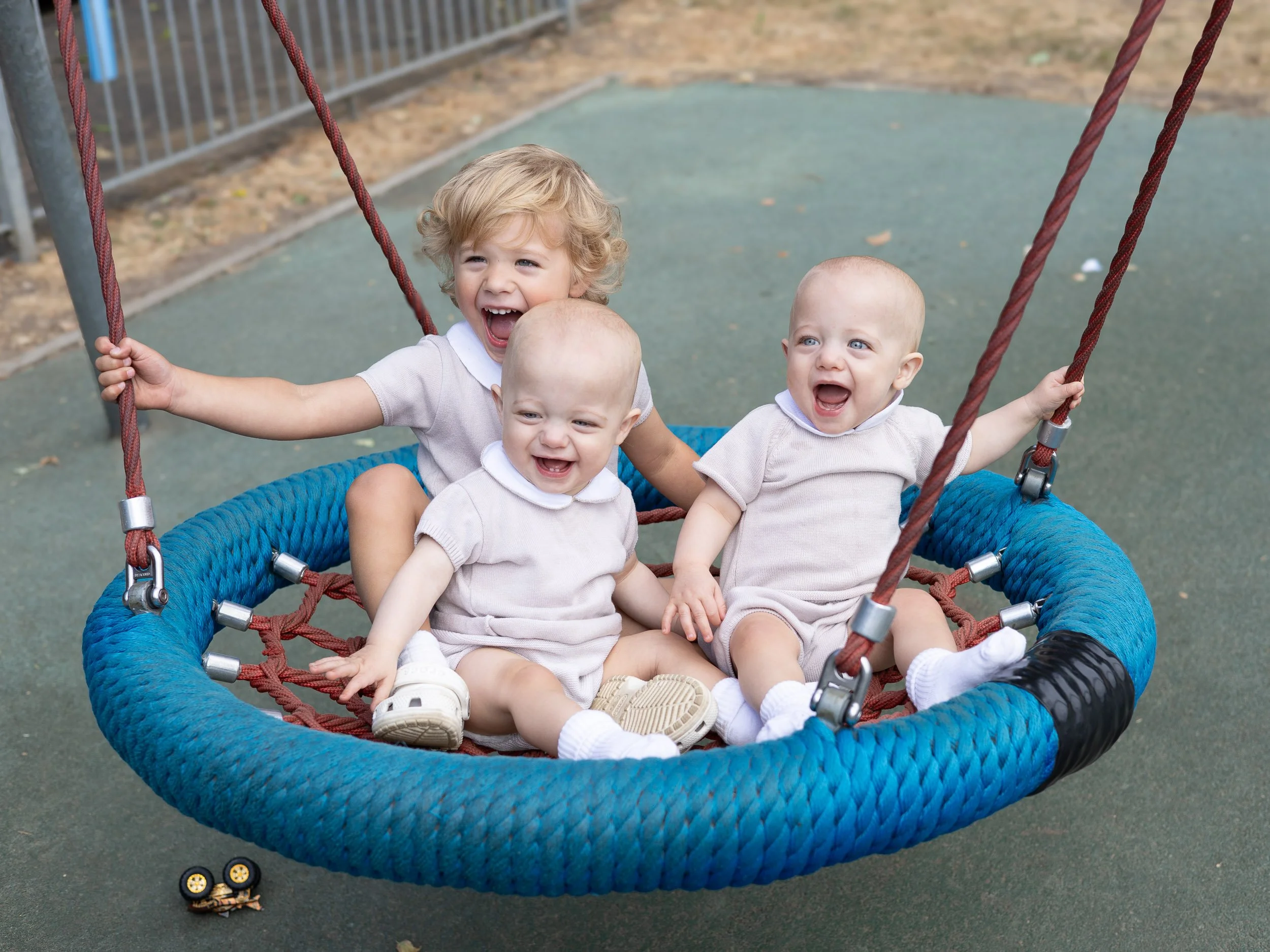 Toddler and his twin brothers laughing while being on the swing during an outdoor photoshoot near me,