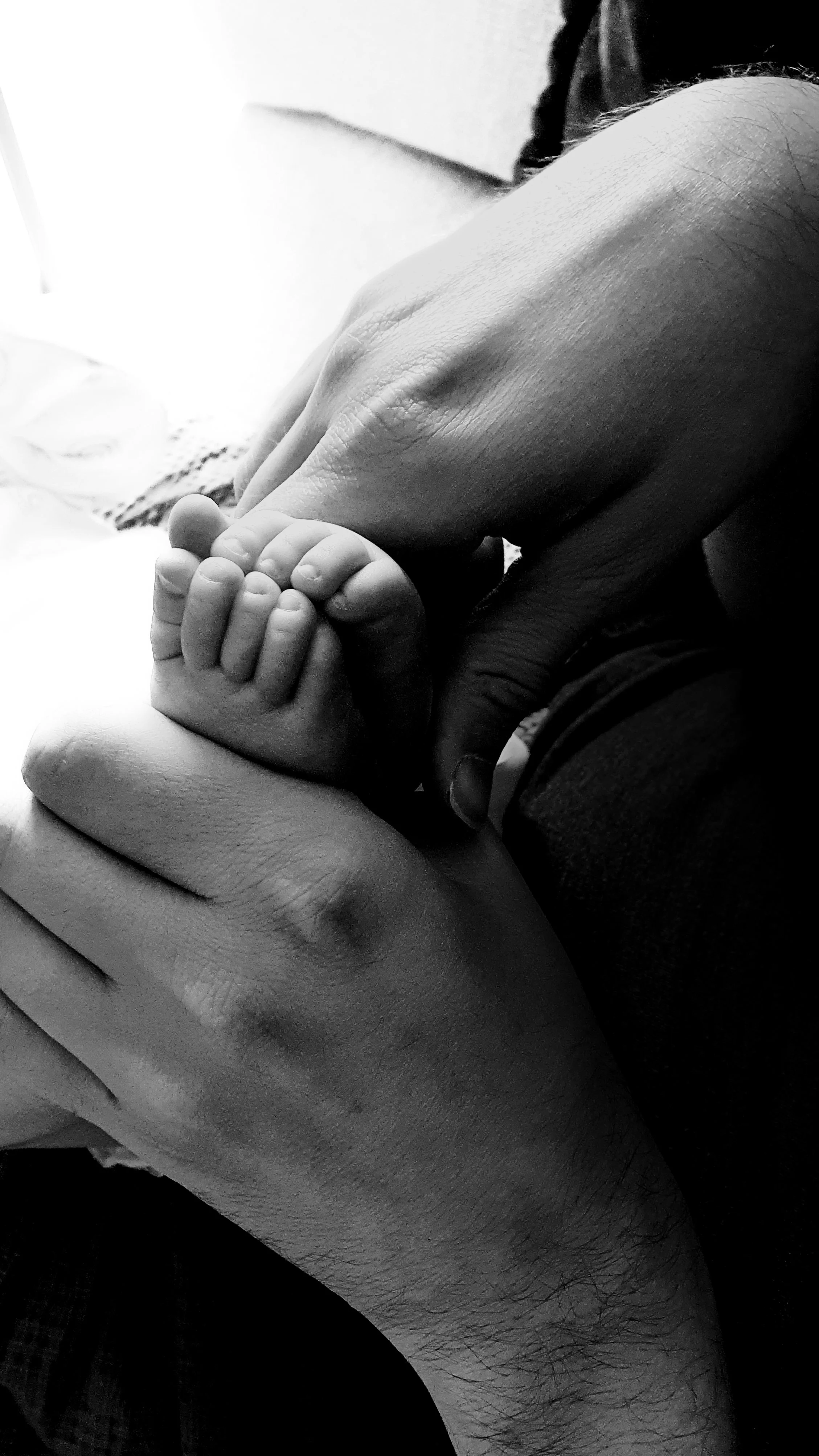 A tender, close-up lifestyle photograph capturing a dad's hands gently cradling his newborn baby's tiny feet.