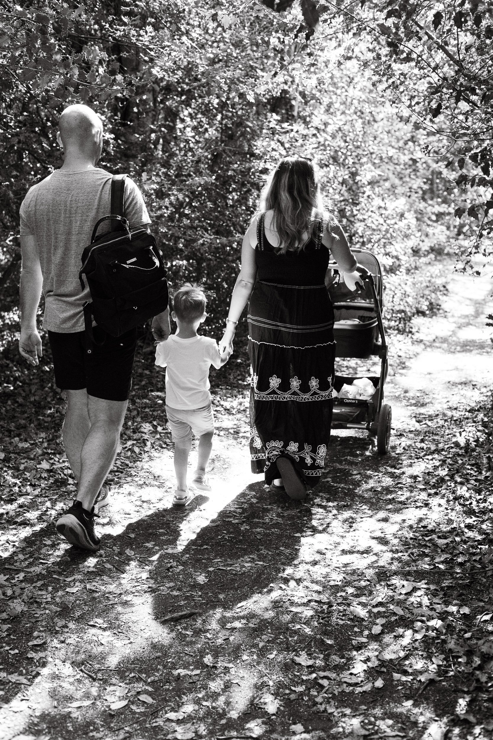 Parents walking along a woodland trail with their young child and stroller during a lifestyle photoshoot near Camberley