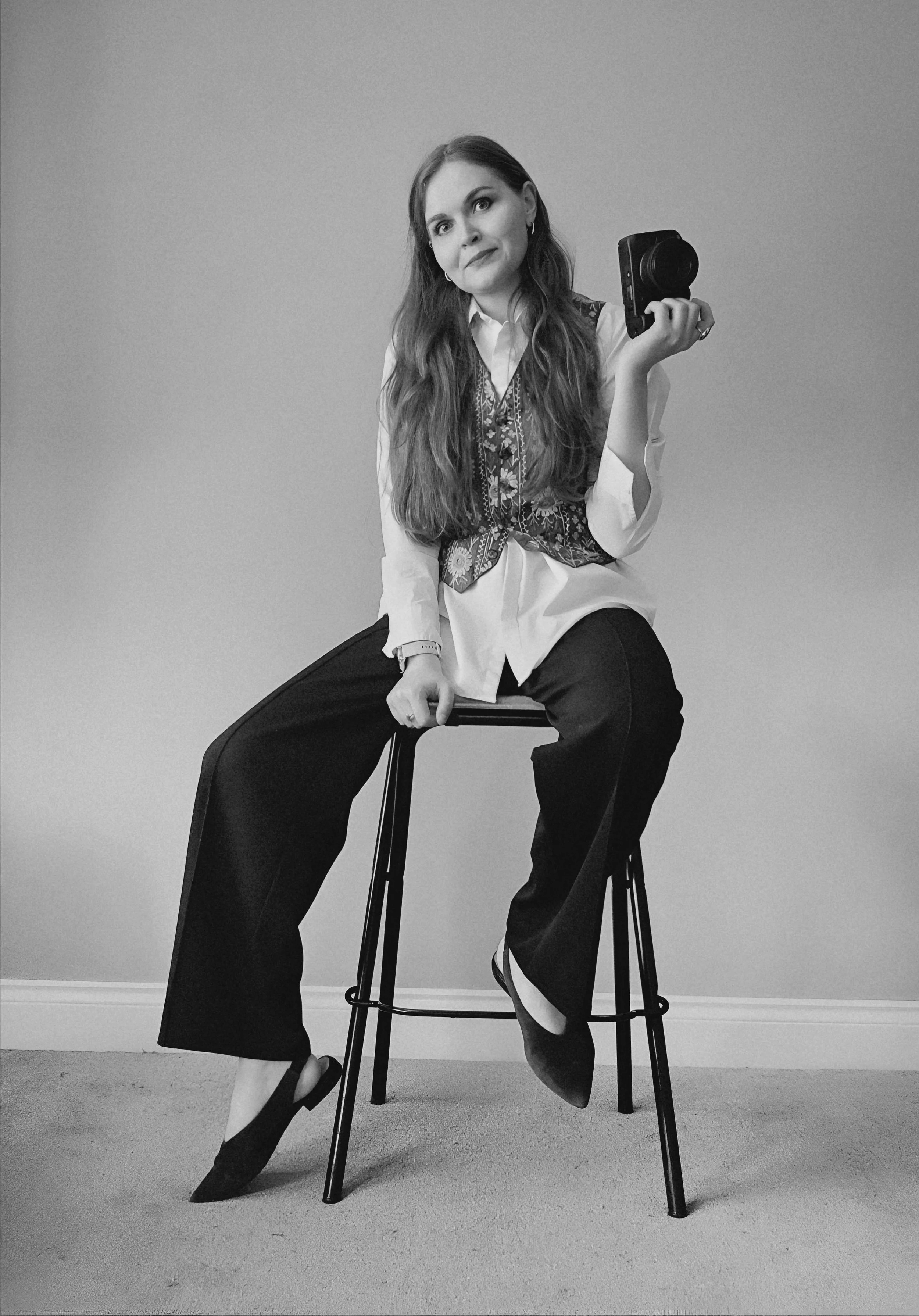 Surrey family photographer Laura holding her camera while sitting on a stool in a bright, natural light photography studio.