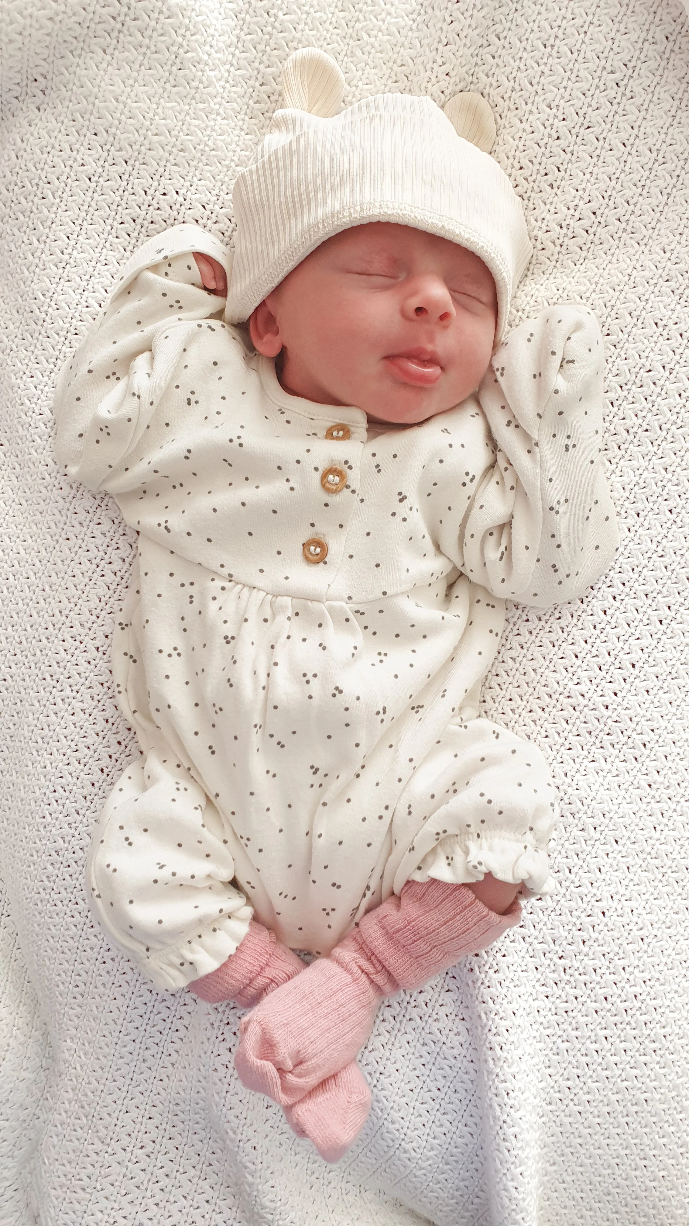 A bright and airy, naturally lit lifestyle photograph of a newborn baby sleeping soundly on a cosy white blanket.