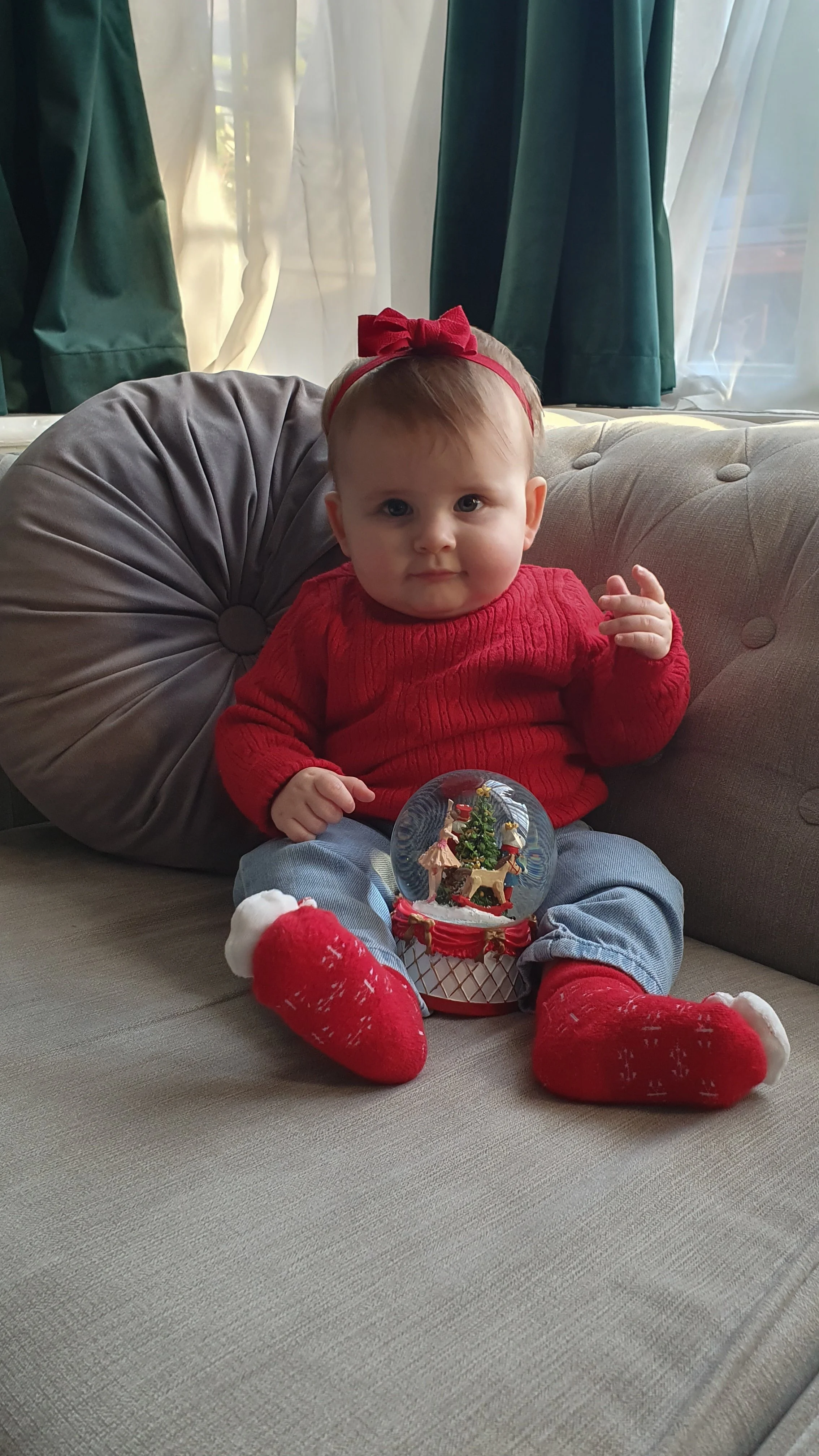A natural, unscripted Christmas lifestyle portrait of a baby sitting on the sofa with a holiday bauble, by a Camberley family photographer..