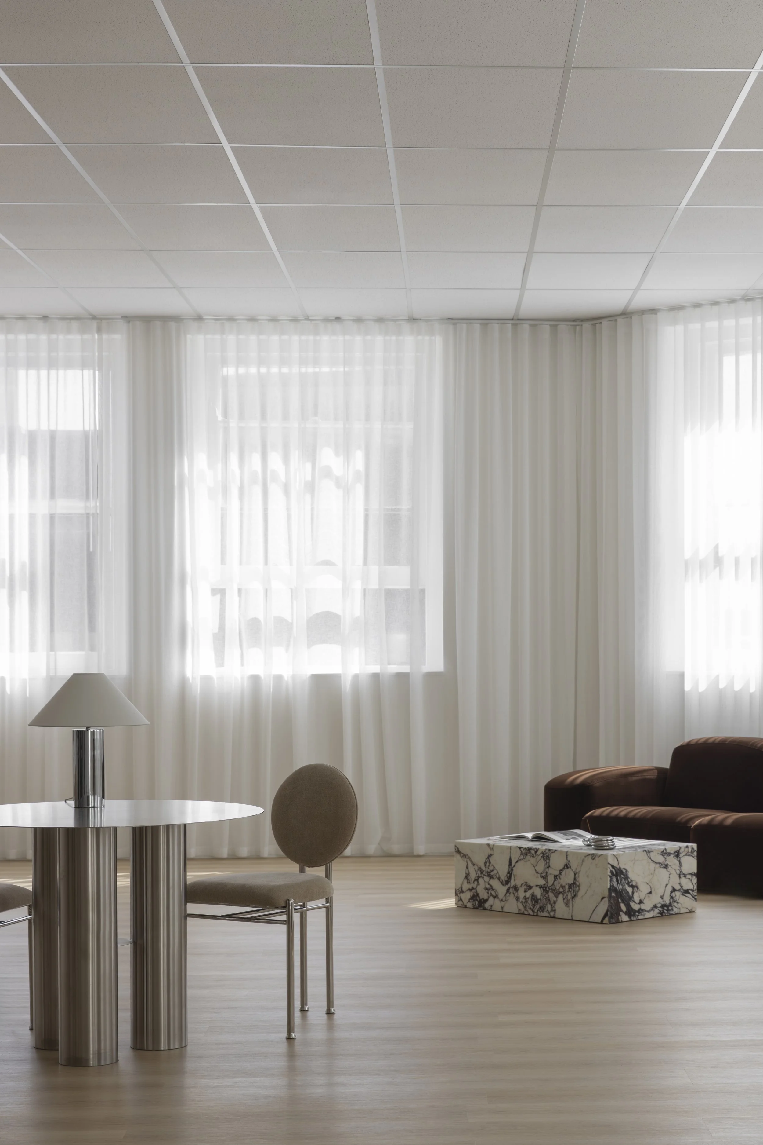 Modern living room with large window drapes, a white round table with a lamp, beige chairs, and brown armchairs, with a marbled coffee table. Content, photography & event studio Newcastle NSW. 