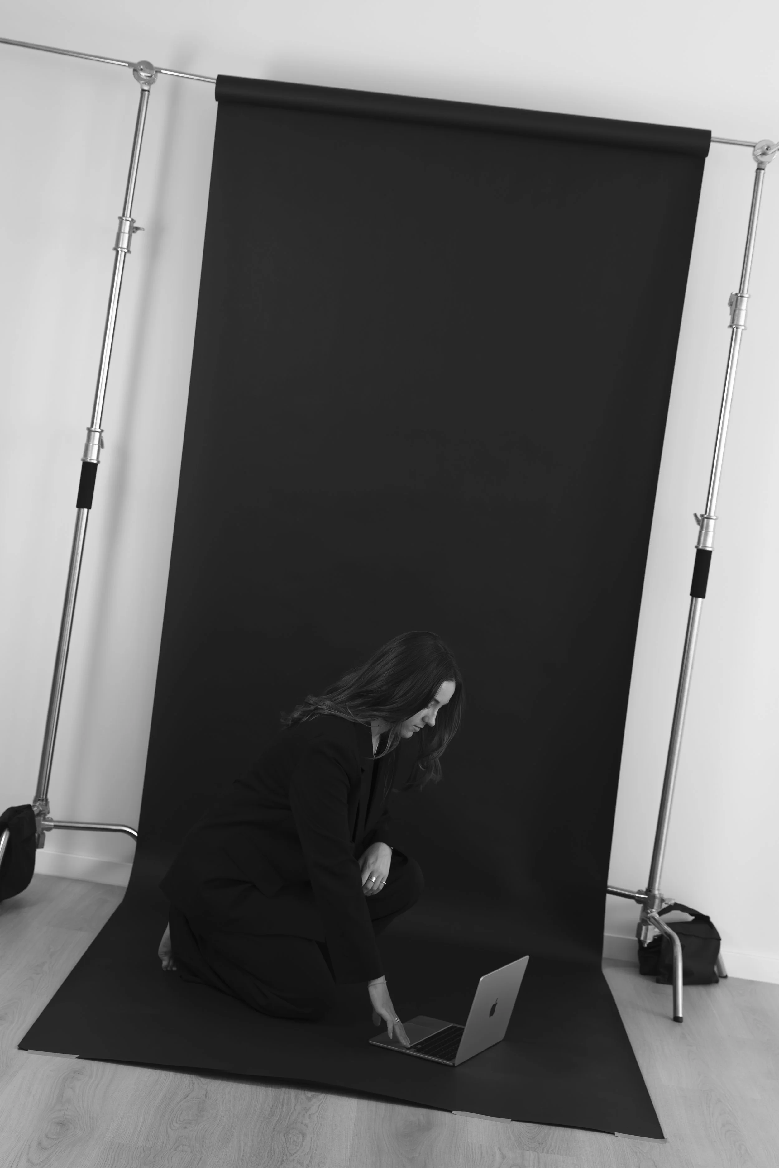A woman is kneeling in front of a black backdrop, adjusting a laptop. She appears to be preparing for a photoshoot or video recording, with professional lighting equipment and a laptop nearby. Content, photography & event studio Newcastle NSW.