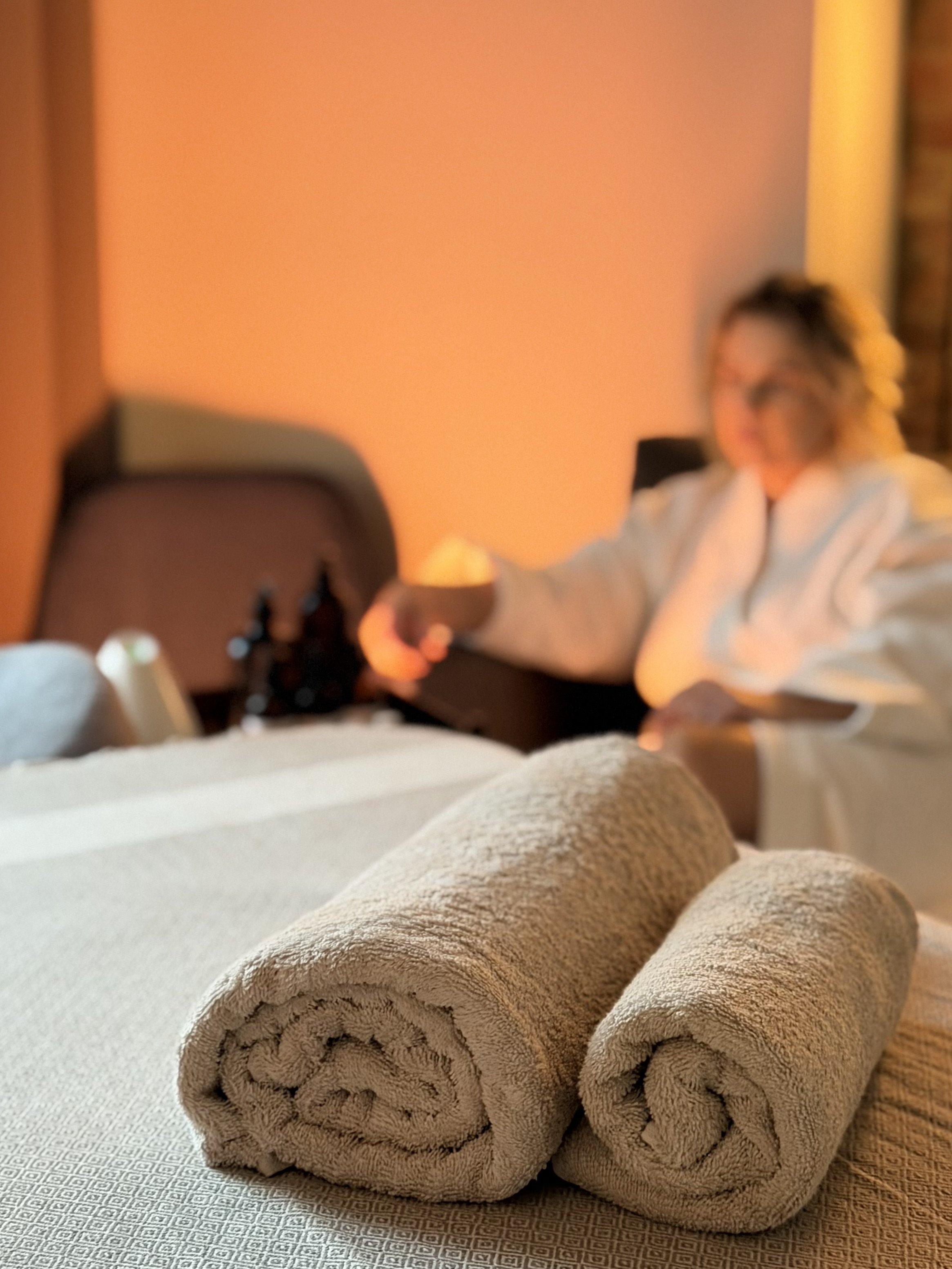 Three rolled beige towels on a textured white shower mat in a bathroom with warm lighting.