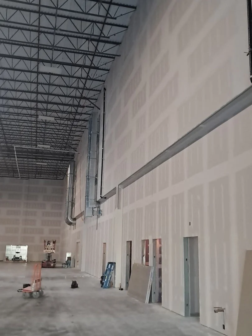 Interior of a large industrial warehouse under construction with demising wall finish taped.