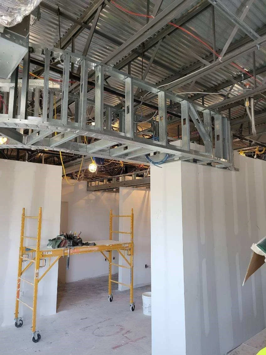 Construction site with metal framework and drywall walls, yellow scaffolding, and exposed ceiling utilities.