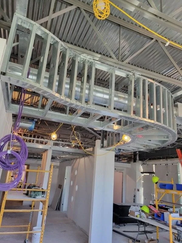 Construction site with metal framework and electrical wiring, with scaffolding, safety helmets, and tools.
