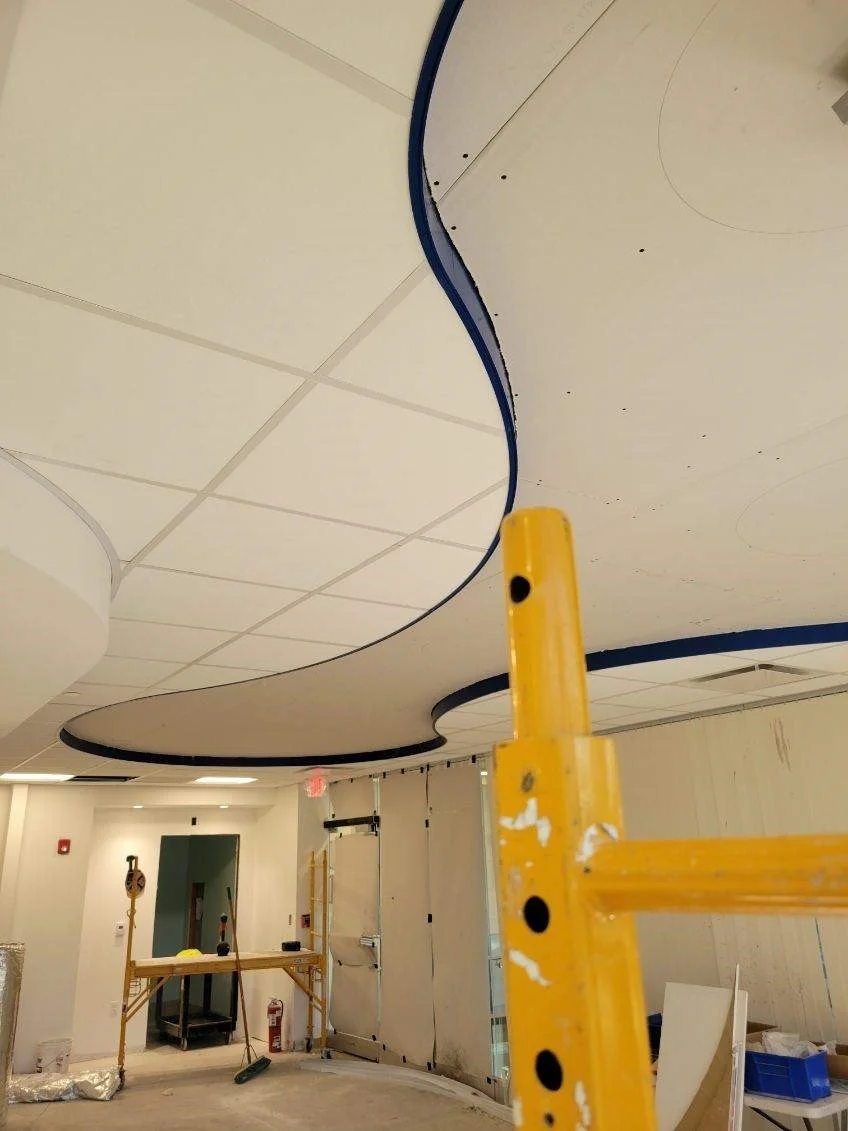 Interior ceiling installation with suspended design, construction tools, and scaffolding in a room under renovation.