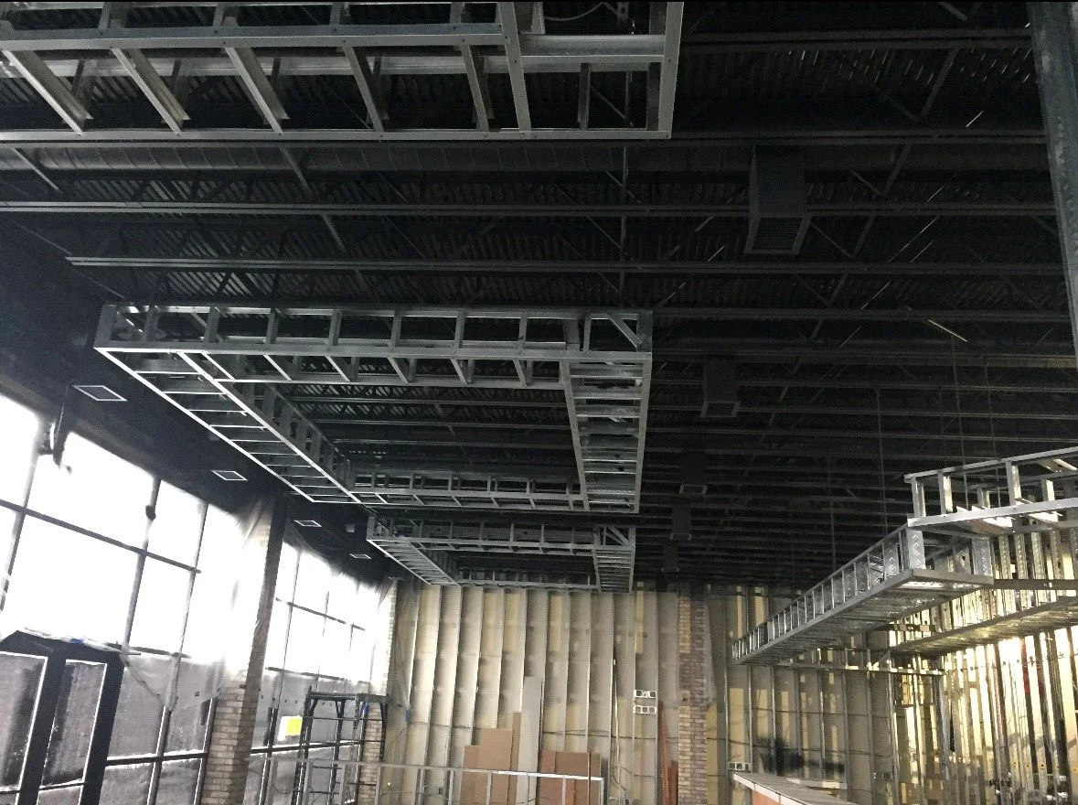 Construction site with black ceiling, metal framework, and large windows, partially built interior walls and scaffolding.