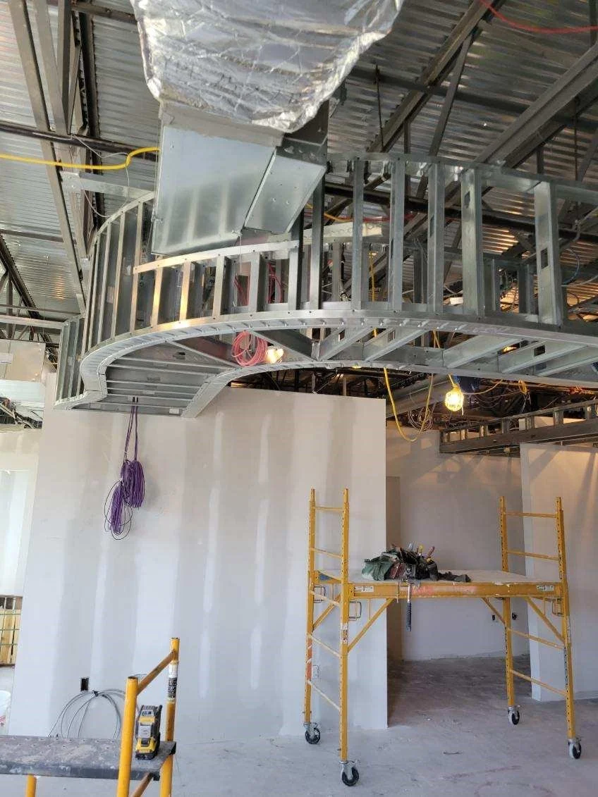 Construction site with metal framework, scaffolding, and a white wall in progress.