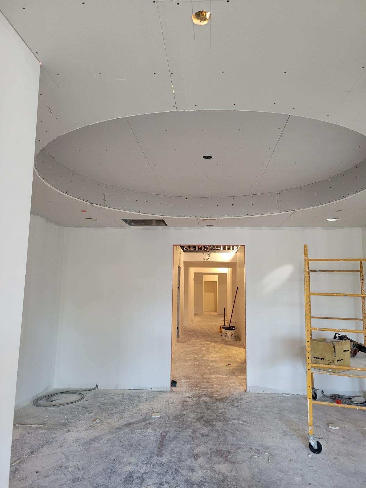 Interior of a building under construction with drywall ceiling, doorway, ladder, and construction tools.