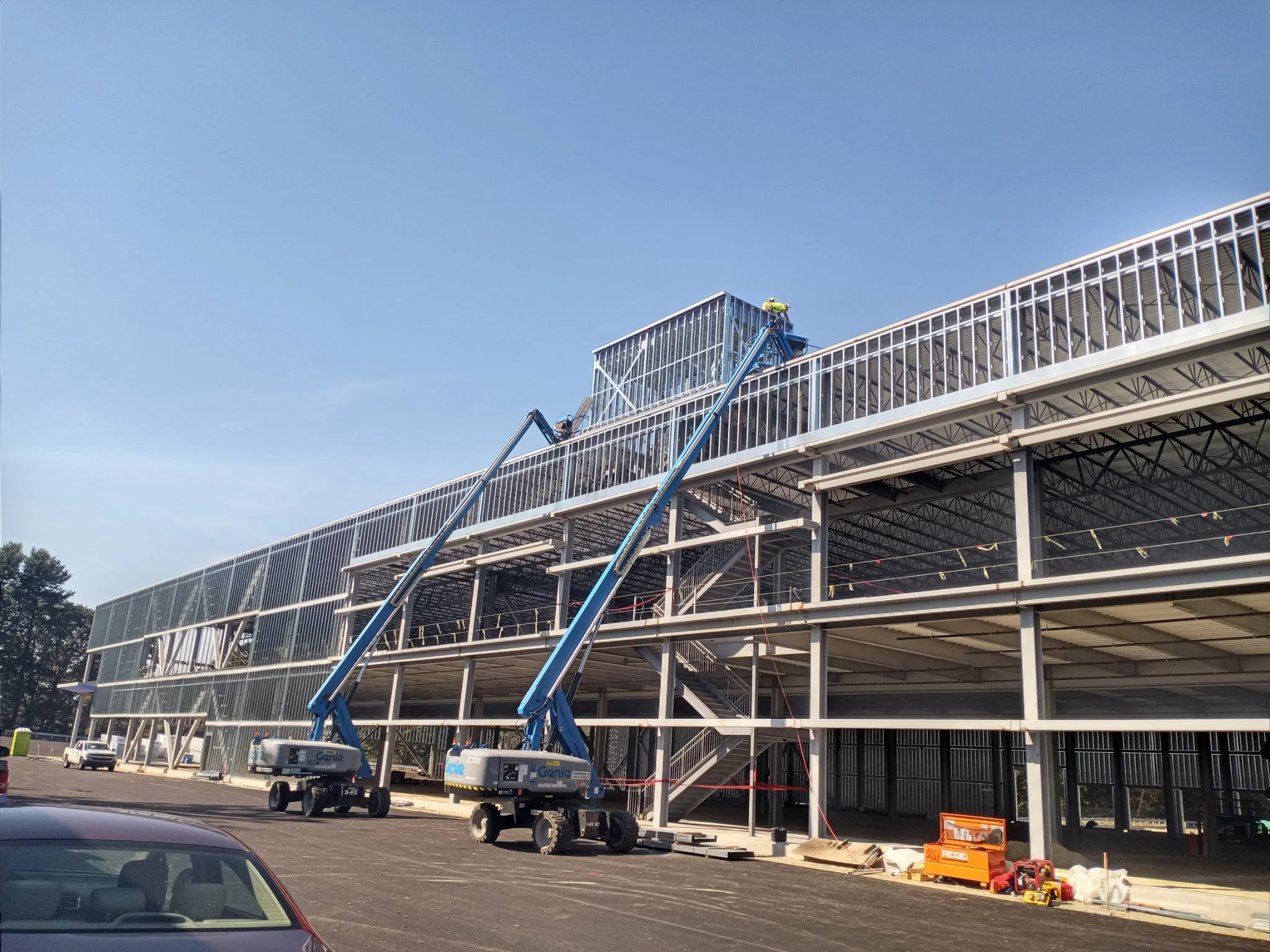 Construction workers on lifts installing the glass facade of a new building, parked cars and construction tools in the parking lot.