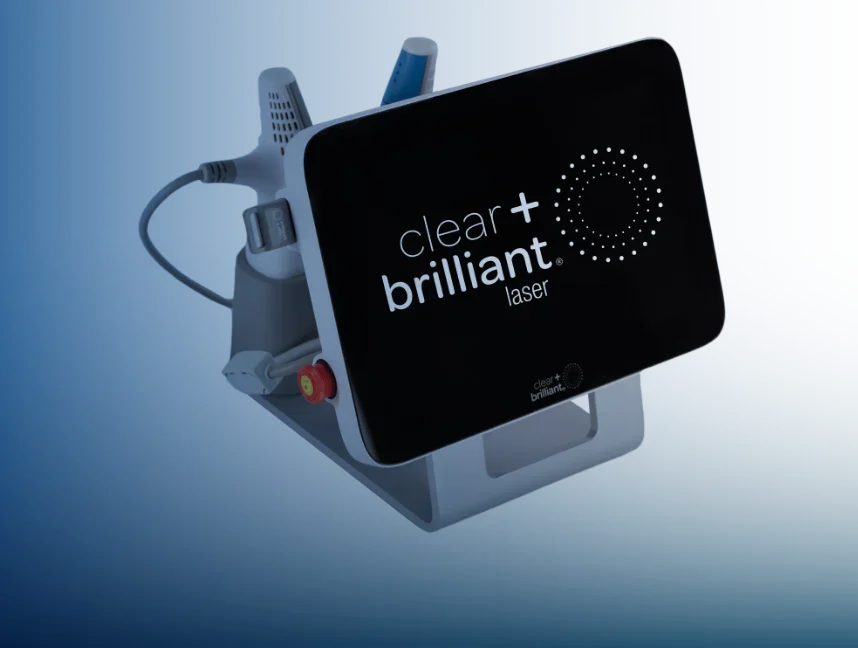 A medical laser device with a black screen displaying the brand 'clear + brilliant laser' and connected to various cords and attachments.
