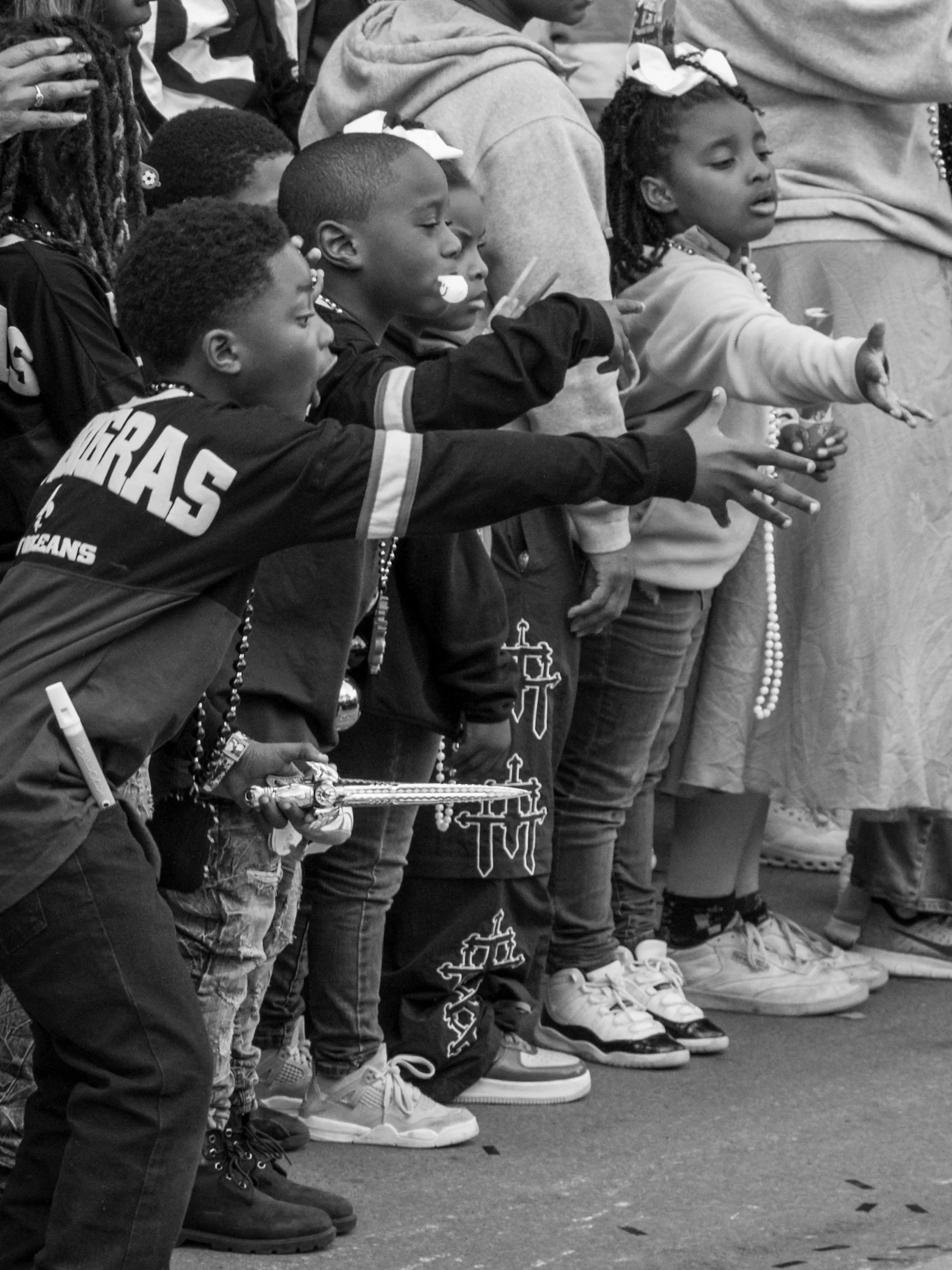 A group of children and adults standing in a row with hands extended forward, participating in a prayer or moment of reflection.