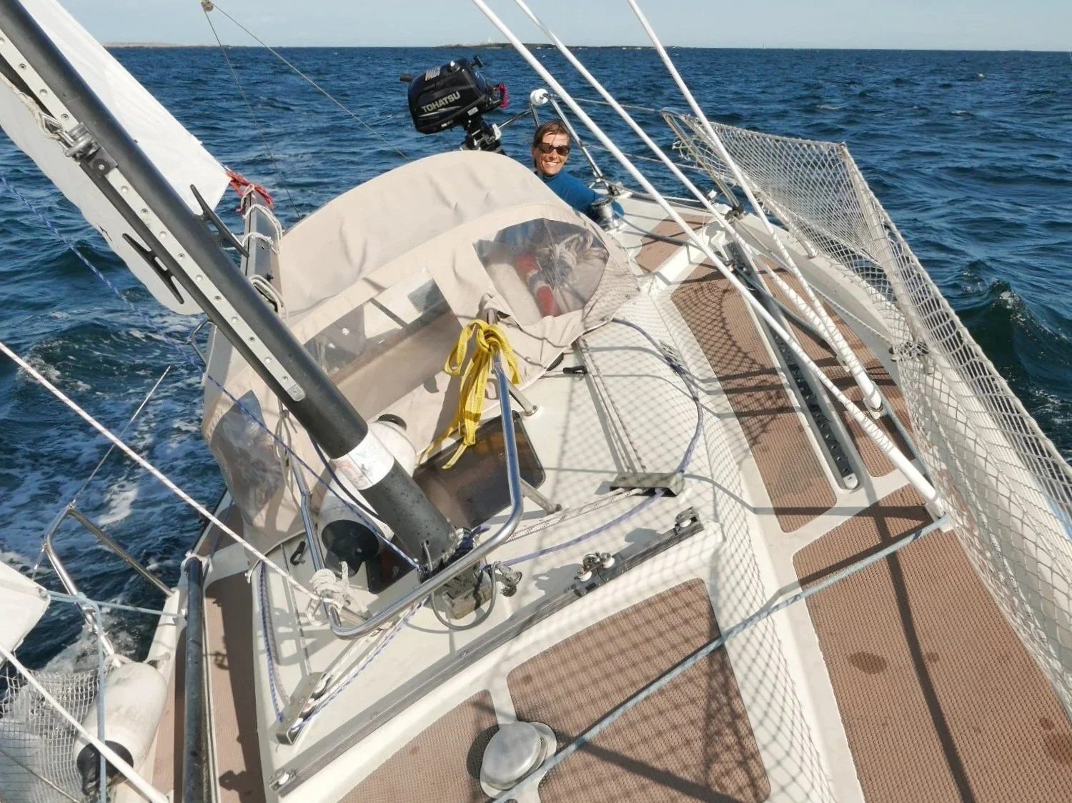 En seielbåt på havet med en person som smiler. Båten ligger skrått i vannet og seiler fint.