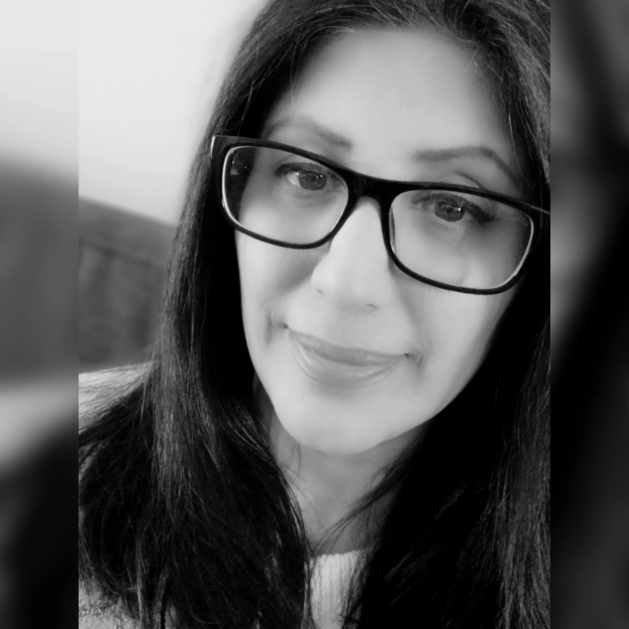 Close-up black and white portrait of a woman with glasses and long dark hair, focusing on her face and eyes.