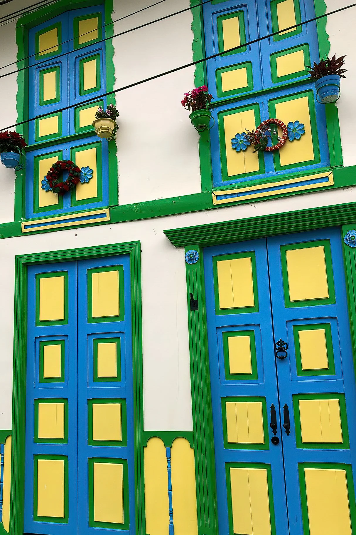 Colorful building with blue and yellow doors and windows, green trim, and decorated with flower pots and wreaths.