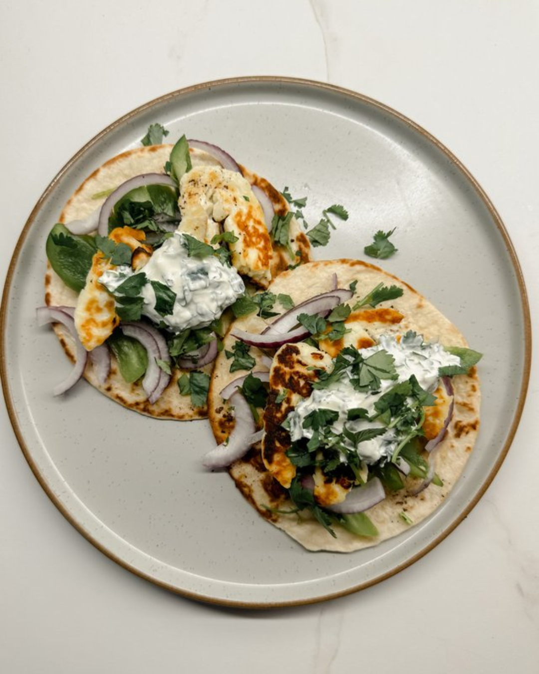 Two tacos on a plate with grilled meat, onions, cilantro, and a dollop of sour cream.