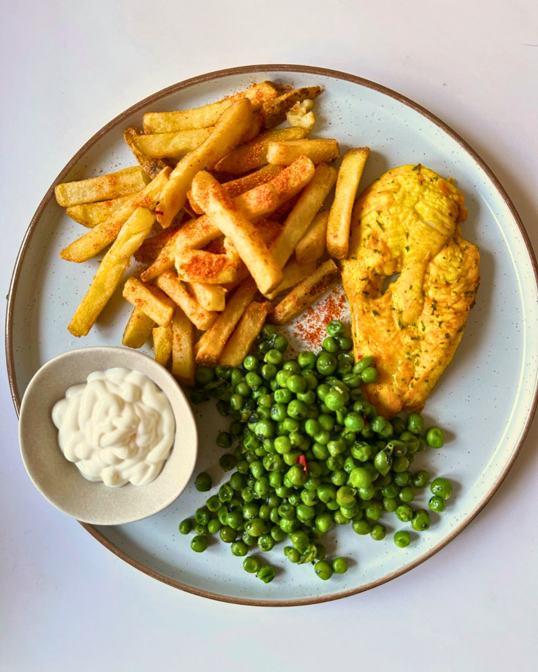 Plate with French fries, seasoned chicken breast, green peas, and a small bowl of mayonnaise.