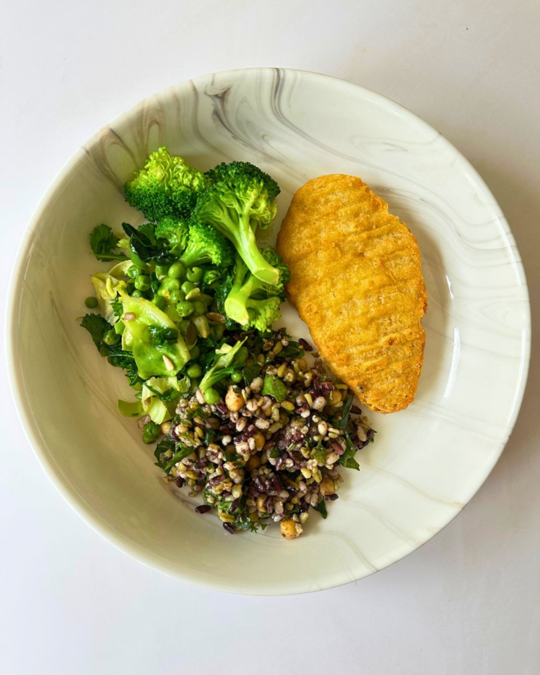 Bowl with broccoli, mixed greens, and grain salad, with a breaded fish fillet.