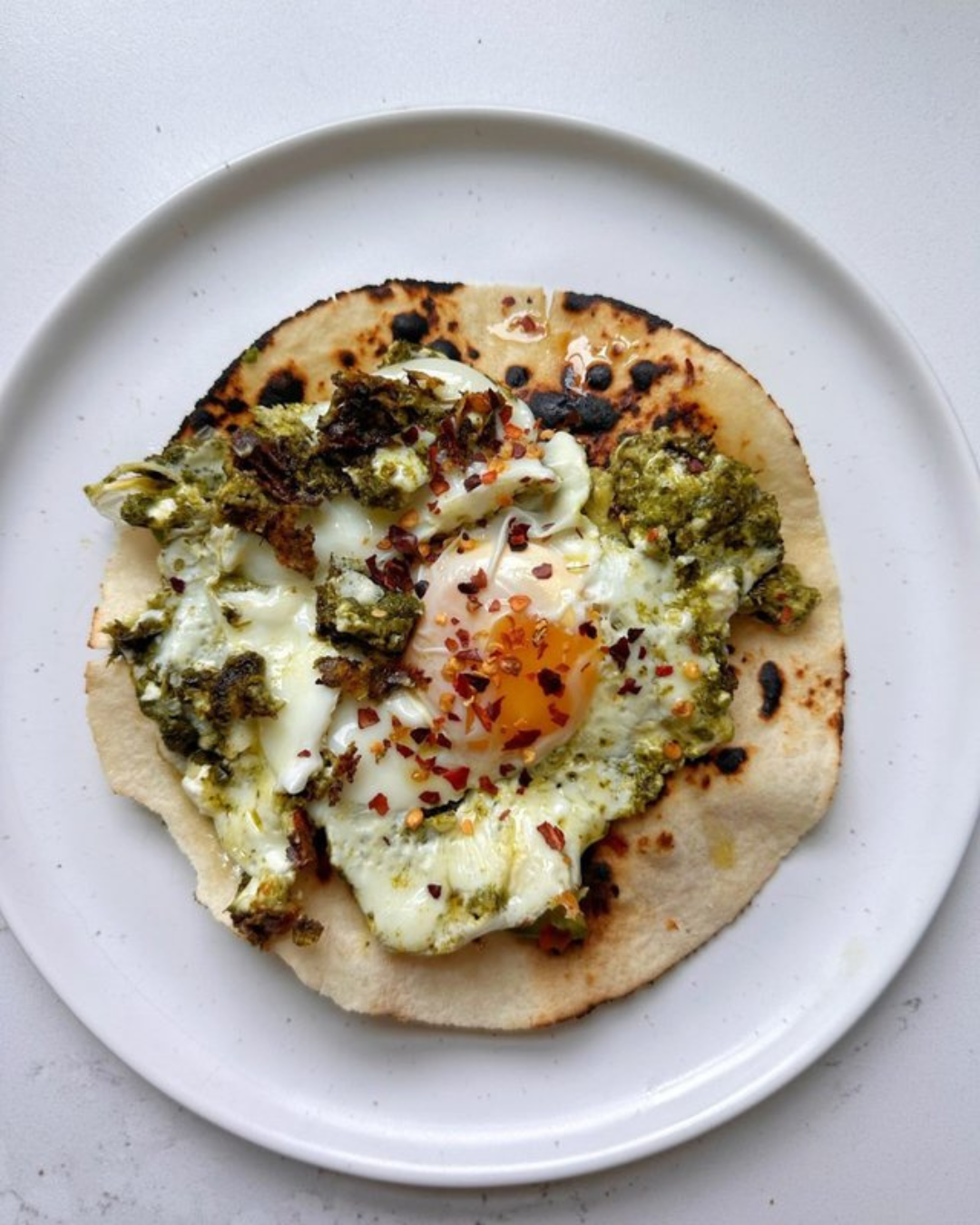 Eggs with green sauce, chili flakes, on naan bread, served on a white plate.