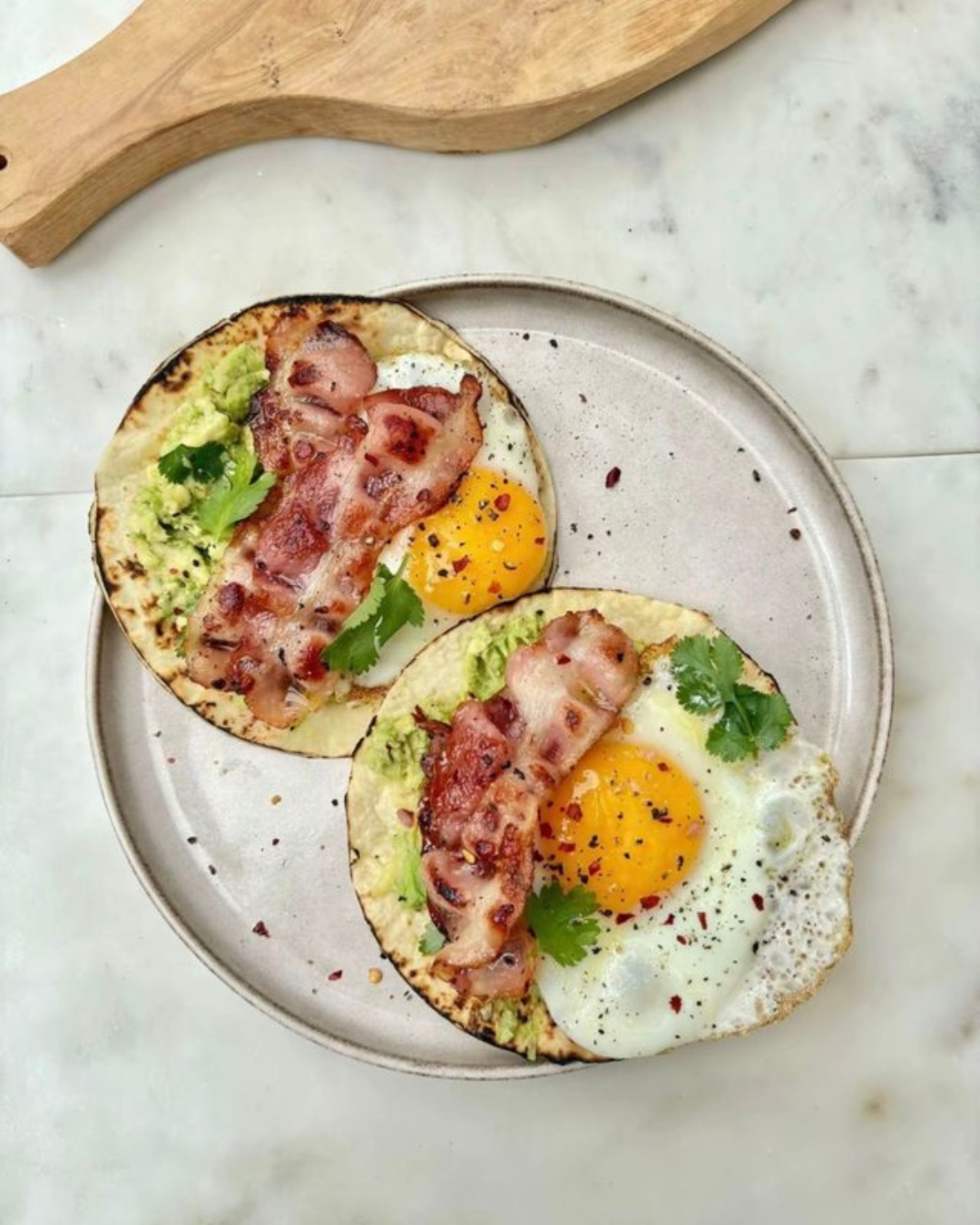 Two fried eggs with bacon, avocado, and cilantro on toasted bread served on a platter.