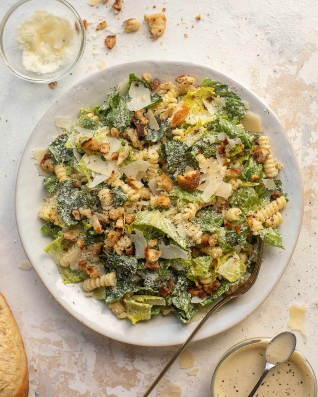 Caesar pasta salad with lettuce, rotini pasta, bacon bits, Parmesan cheese, and creamy dressing with black pepper.