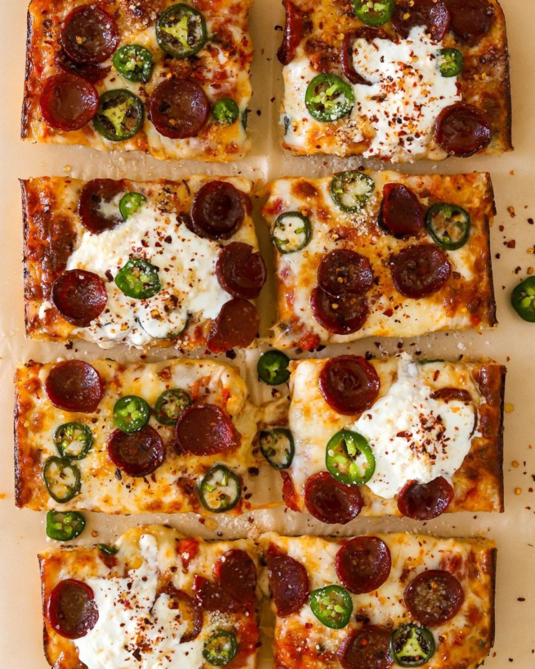 Six slices of pepperoni pizza topped with jalapeño slices and sprinkled chili flakes on a beige surface.