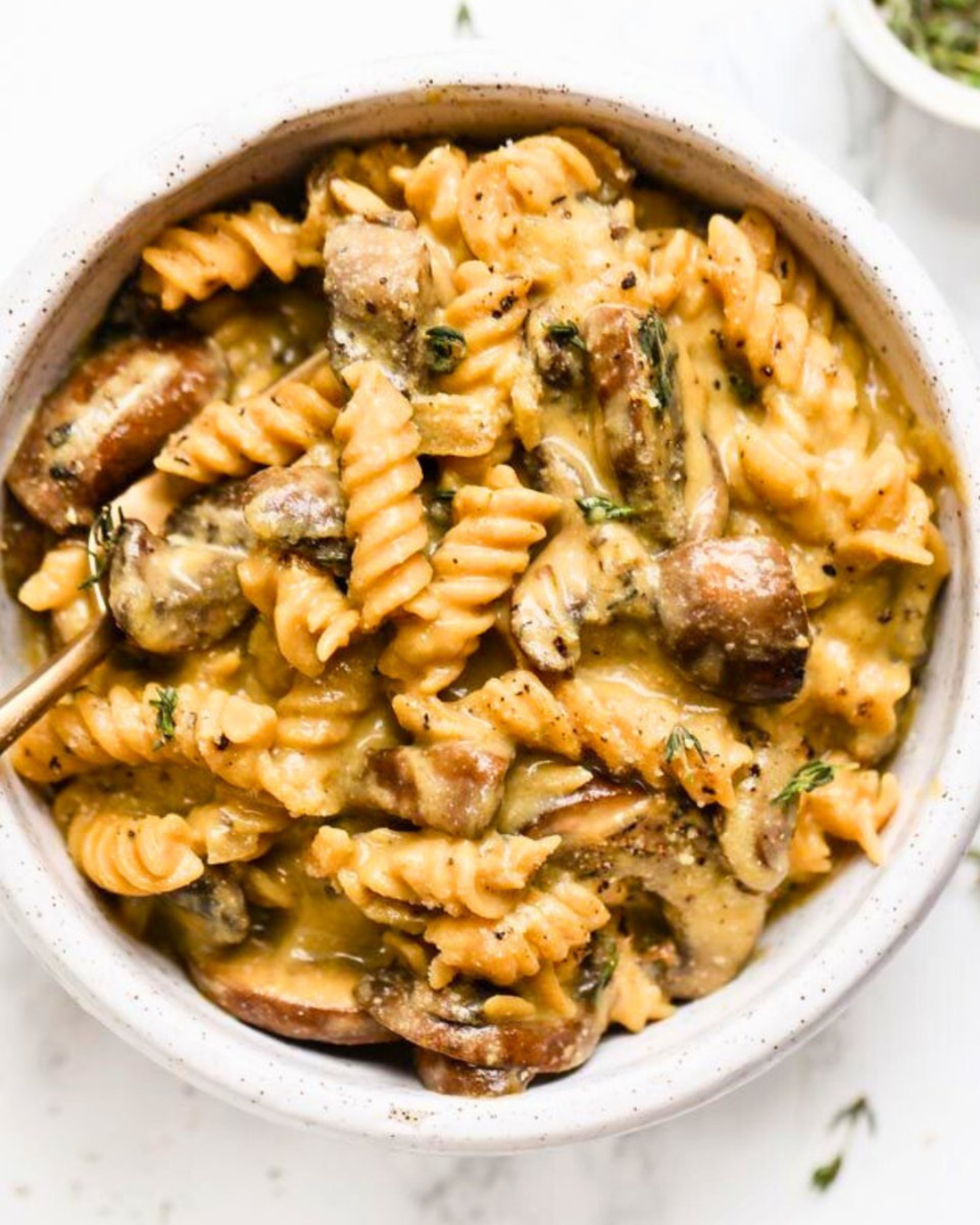 A bowl of creamy pasta with mushrooms, sausage, and herbs.