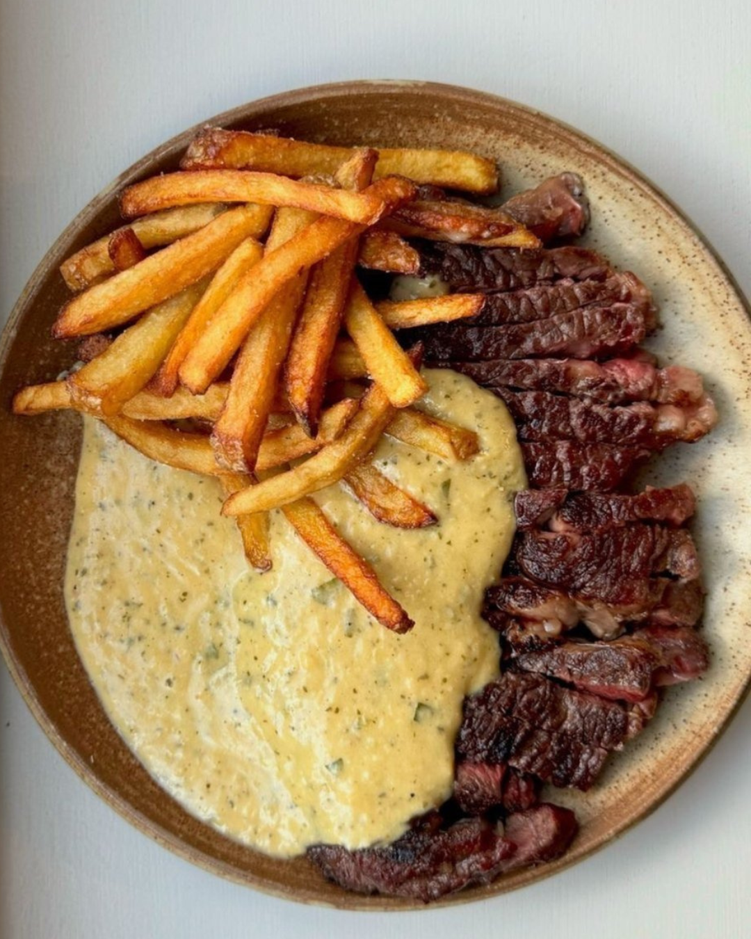 Plate with French fries, sliced steak, and creamy yellow sauce.