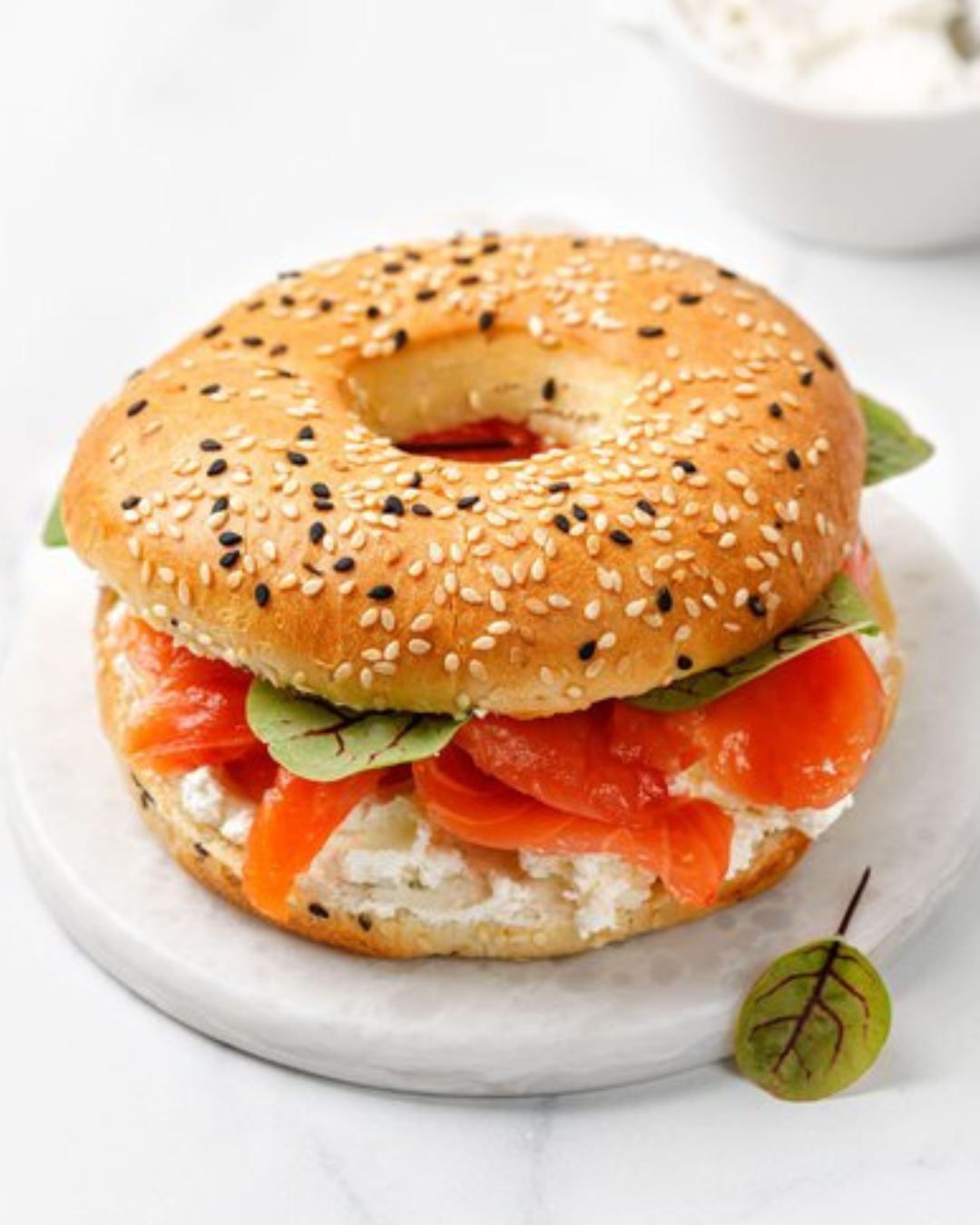 Bagel sandwich with smoked salmon, cream cheese, and greens on a marble board.