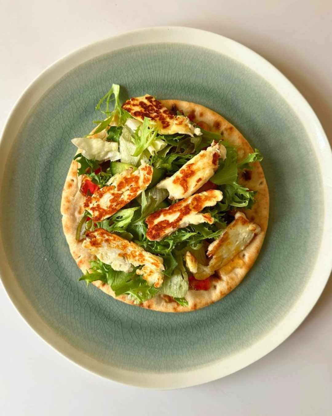 Salad with grilled chicken slices, lettuce, and tomato, served on a flatbread on a light green plate.