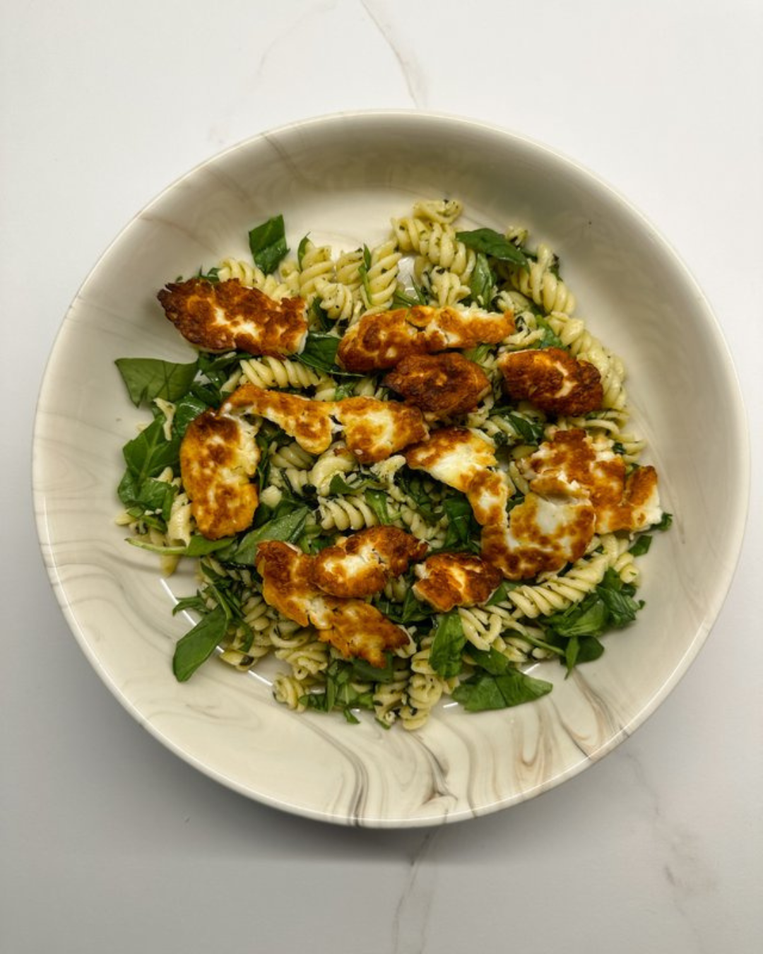 Pasta salad with rotini pasta, chopped greens, and grilled chicken slices in a white bowl.