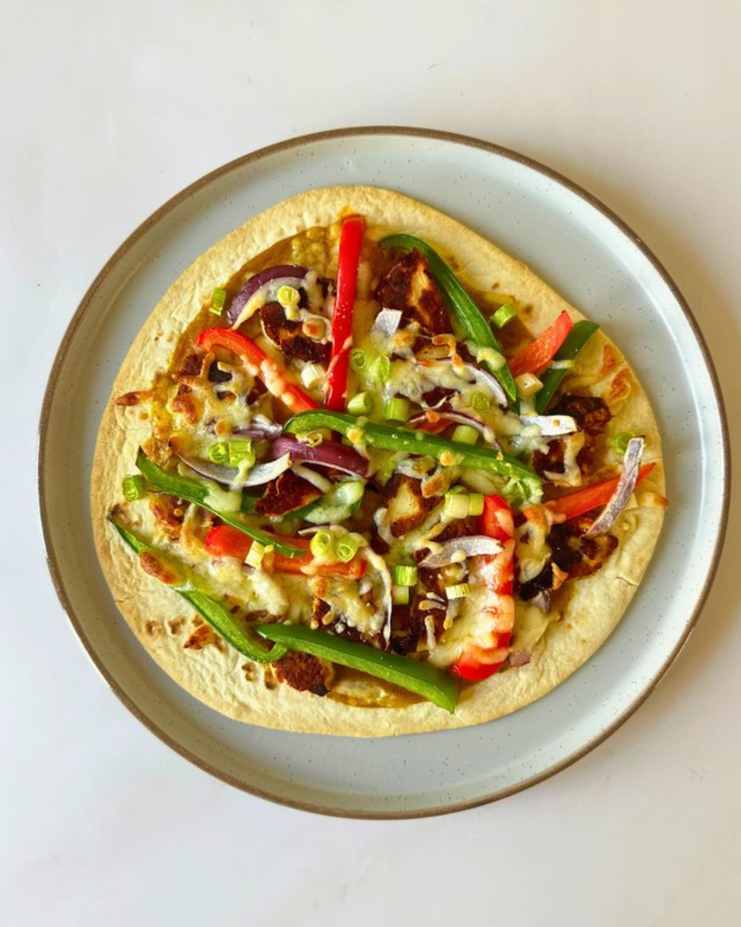 A taco with sliced tomatoes, red and green bell peppers, onions, shredded cheese, and meat on a white plate.