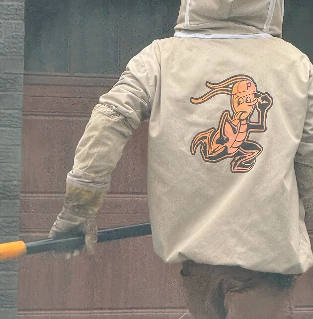 Brian Essek of Pests Go Home Pittsburgh wearing a beige jacket with a cartoon character on the back, holding a tool, possibly a broom or rake, working outdoors.