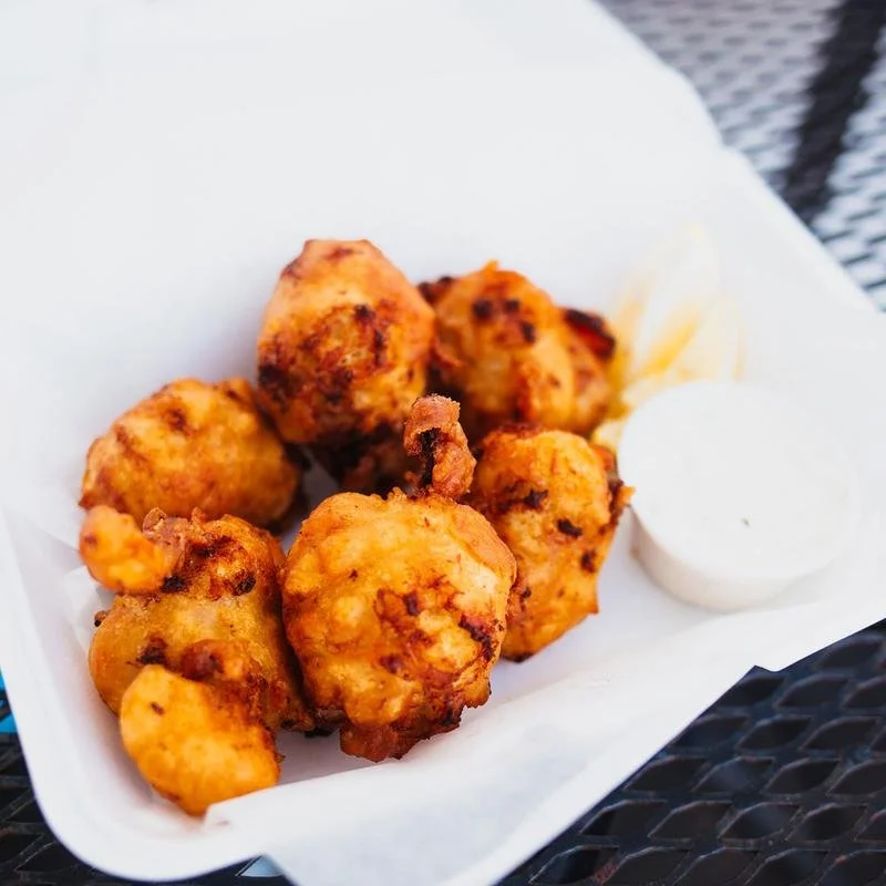 Clam cakes with dipping sauce in a white takeout container.