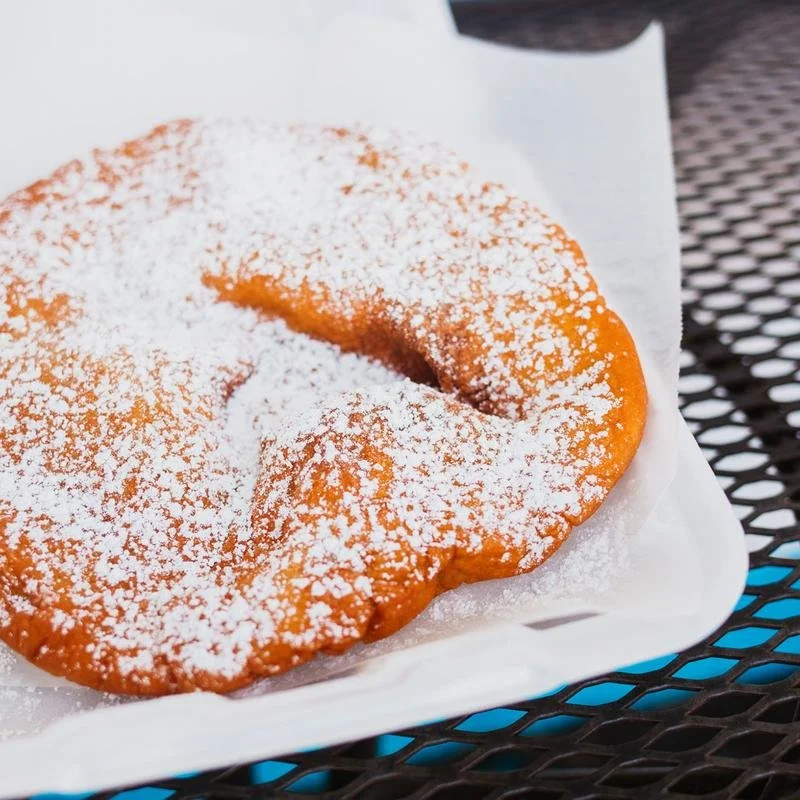 A fried pastry dusted with powdered sugar on white paper on a black metal table.
