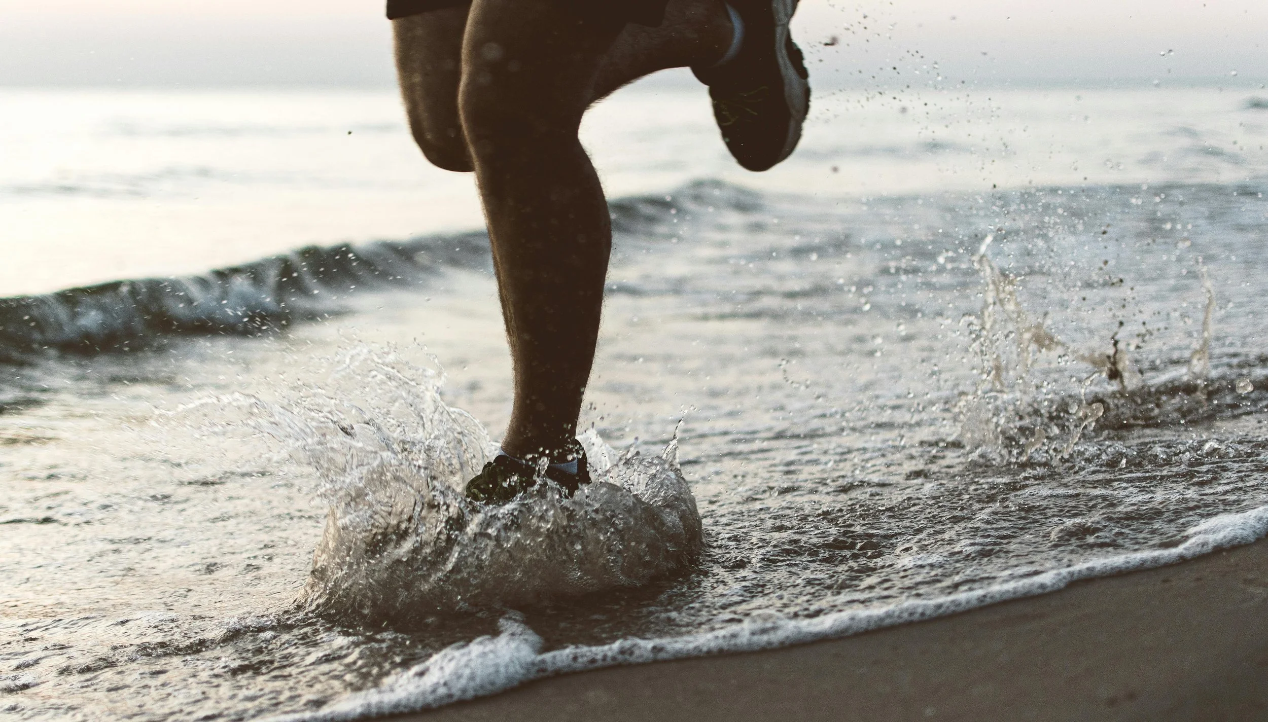 Runner splashing through shallow water on a Sunshine Coast beach at sunrise
