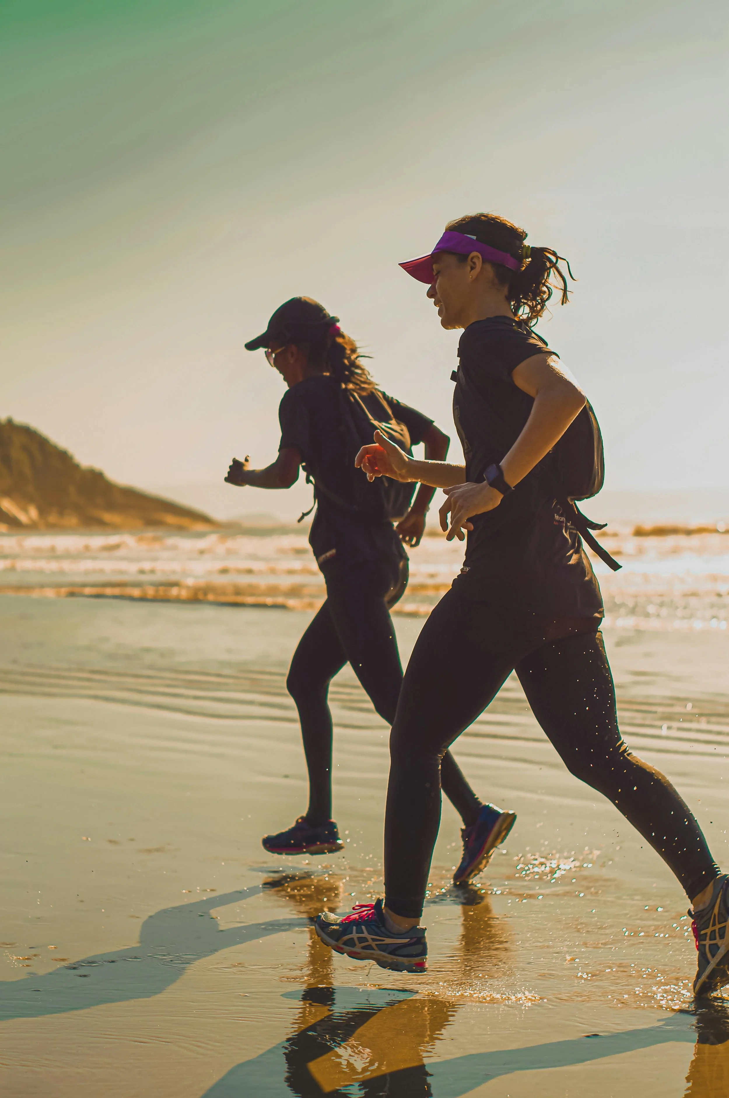 Two women trail running along the beach at sunrise wearing athletic shoes