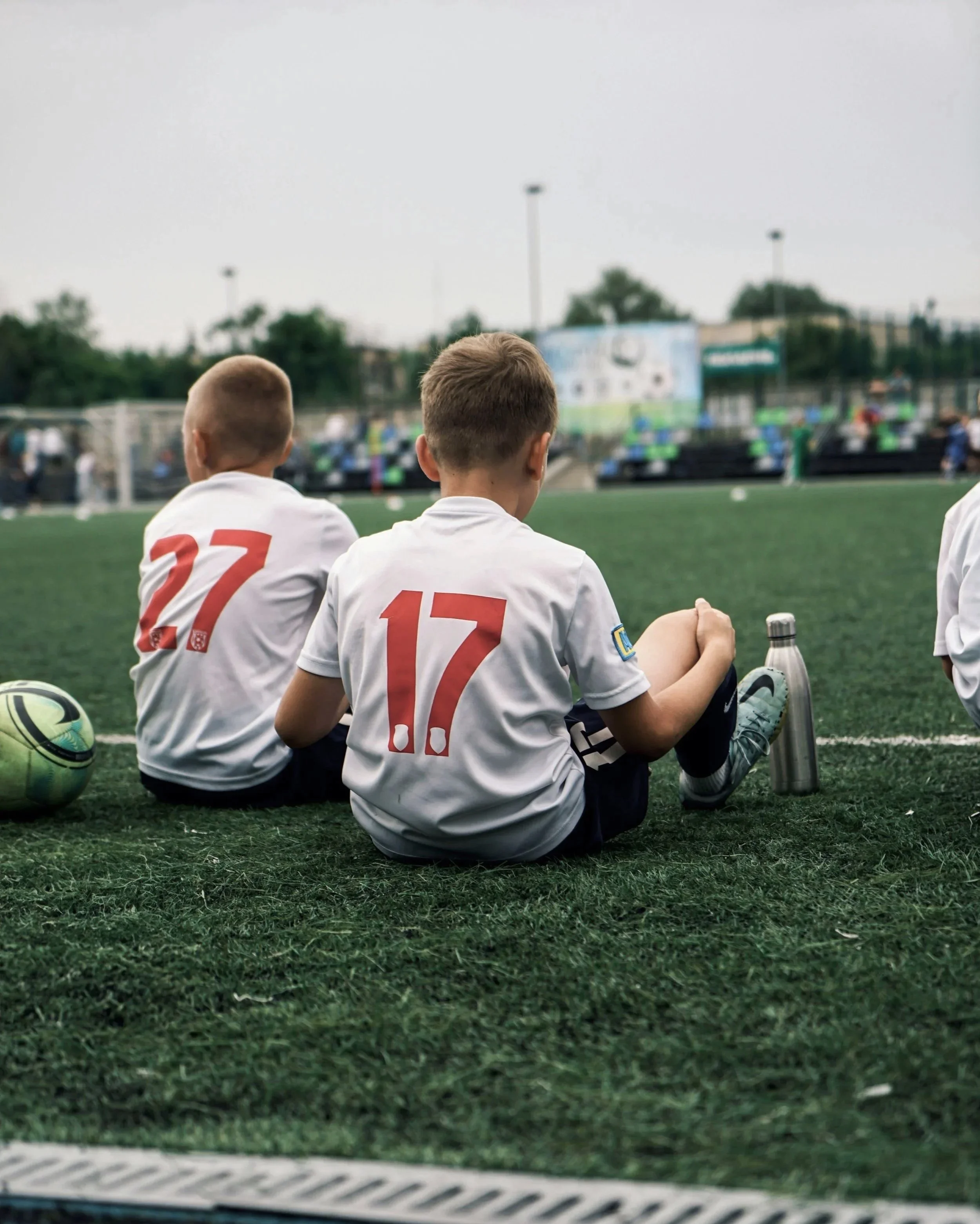 Two children in soccer uniforms sitting on sidelines at kids soccer game on the Sunshine Coast