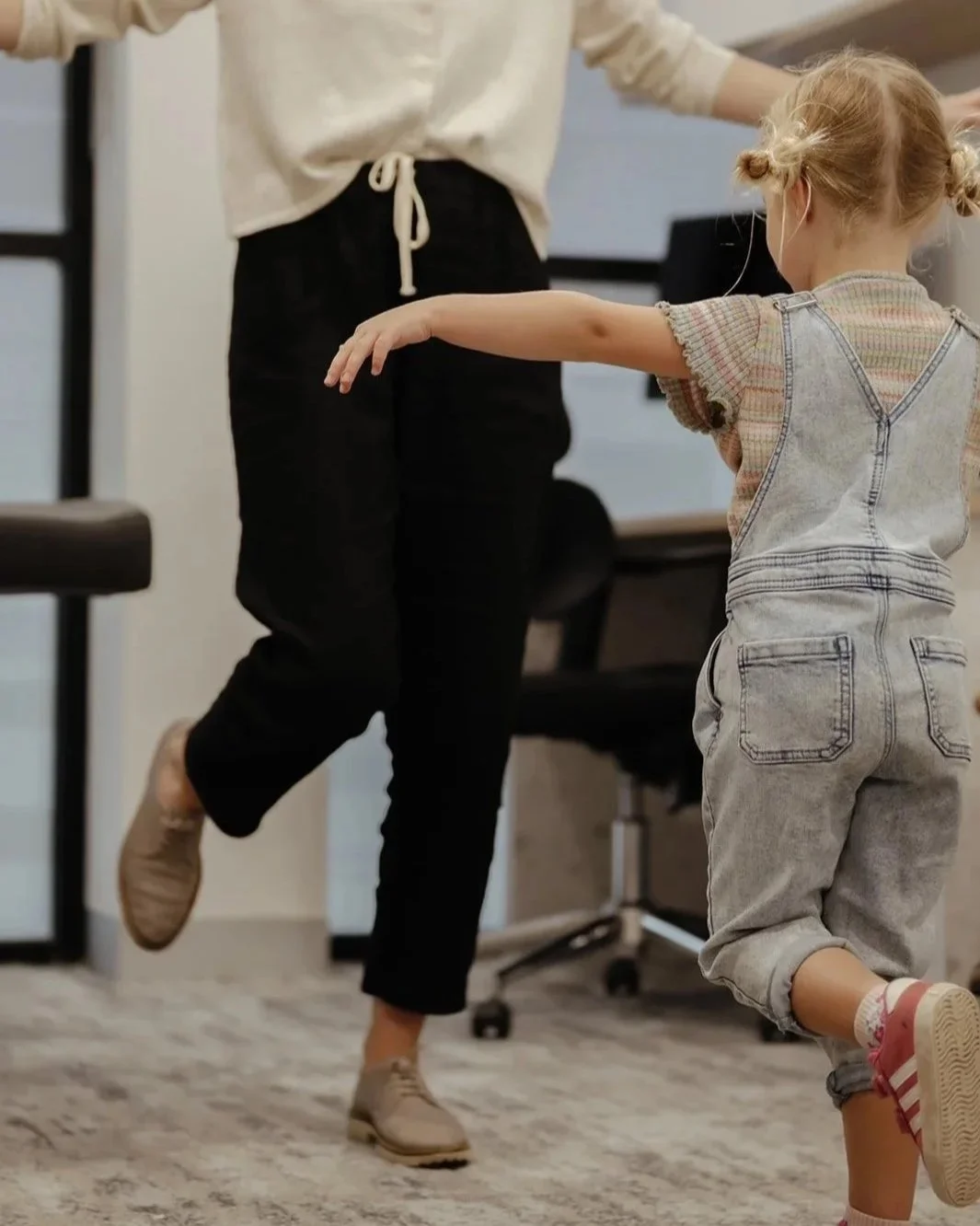 Child standing and balancing on one foot having a podiatry assessment with podiatrist in background mirroring the exercise.