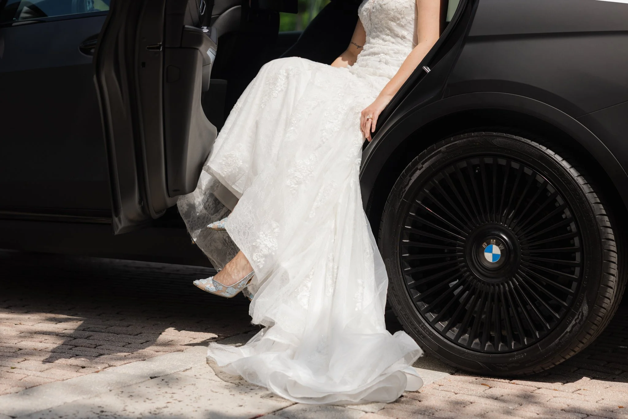 Bride in a wedding dress stepping out of a black BMW car.