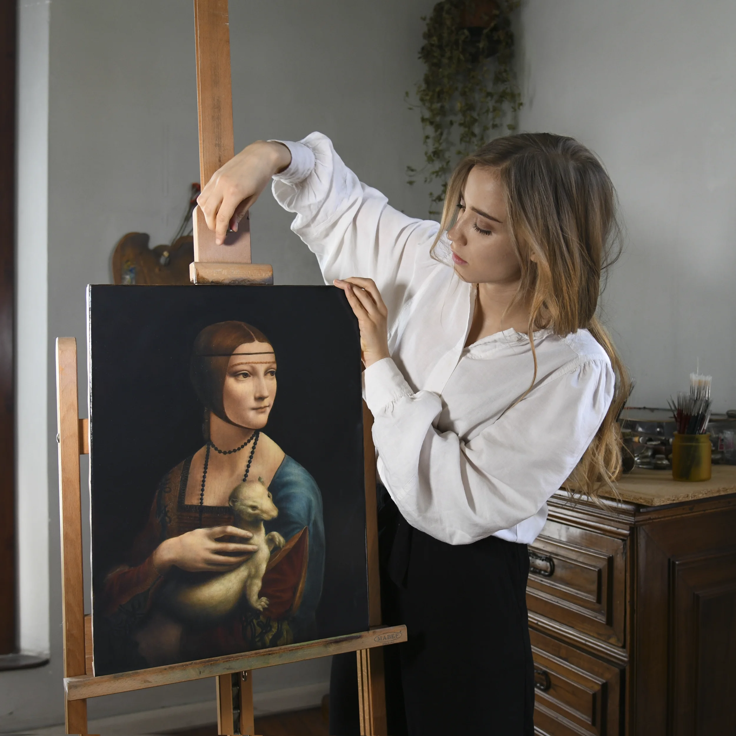 Artist Anna Sumislawska in her studio adjusting her reproduction of Leonardo da Vinci’s Lady with an Ermine on an easel.