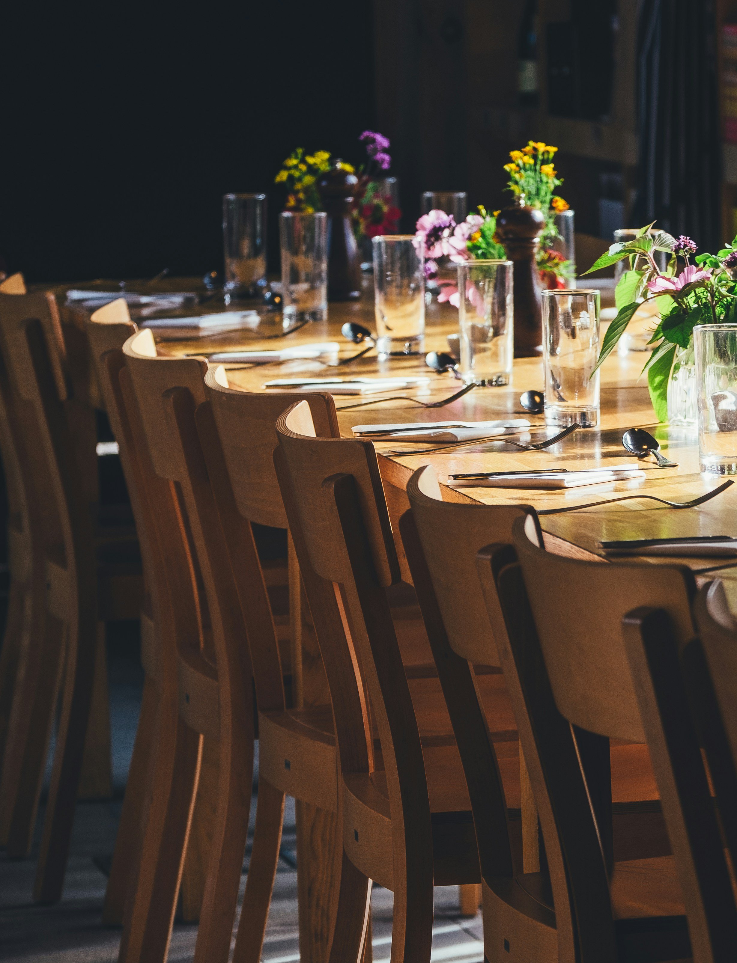 Empty dining table set with glasses, silverware, napkins, and colorful flower arrangements in a restaurant or banquet hall.