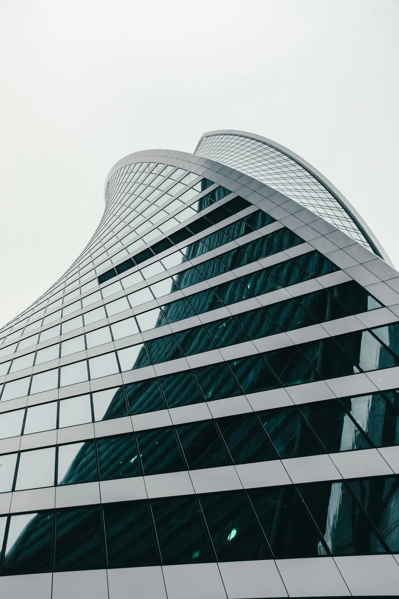 A tall, modern skyscraper with a curved glass facade reflecting the sky, taken from a low angle.